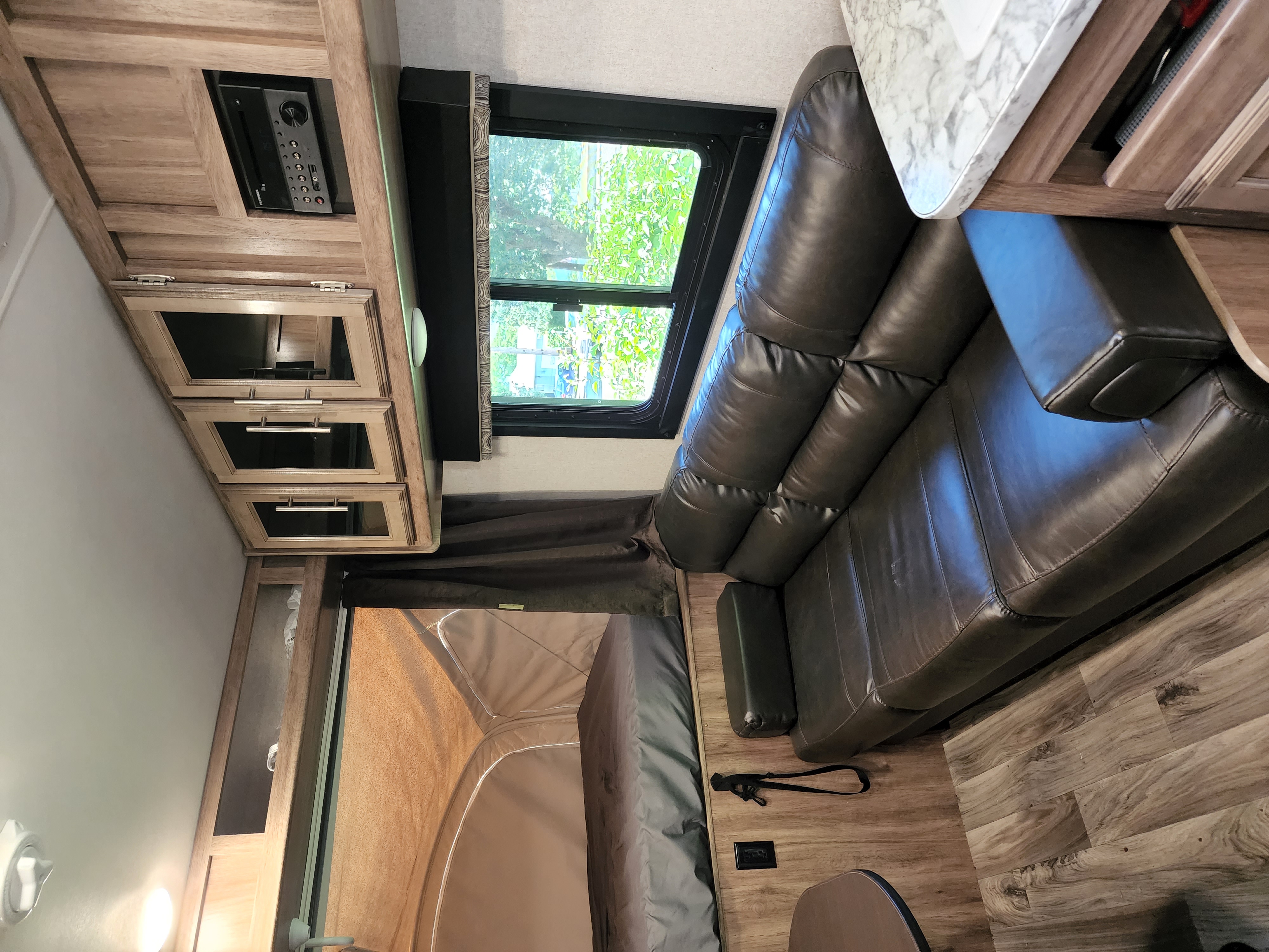 This RV rental's cozy interior features a dark leather sofa, entertainment system, window, and wood-look flooring.. Jayco Jay Feather 2018