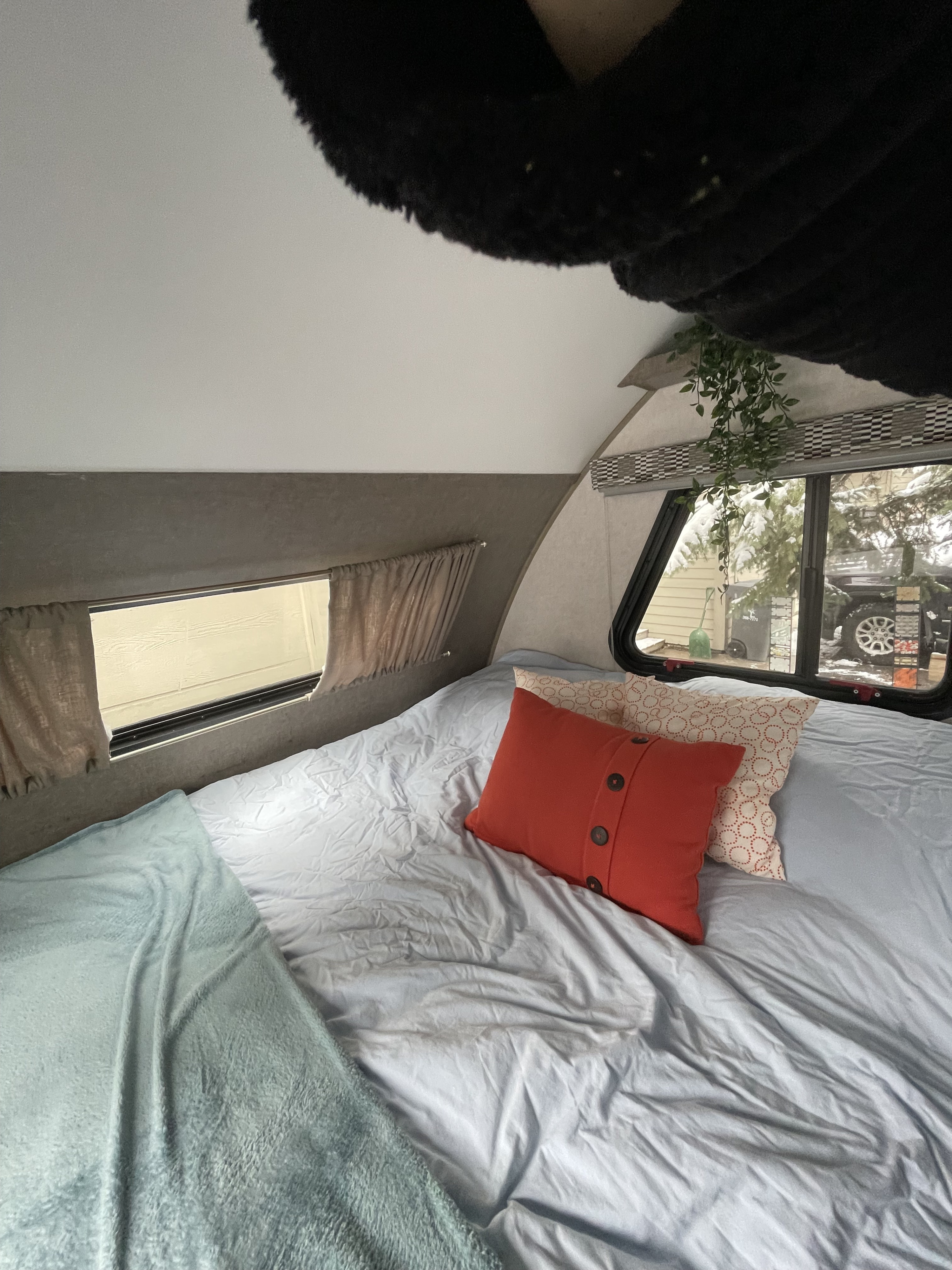 A comfortable RV rental bedroom with a neatly made bed, decorative pillows, and a window offering a glimpse of a snowy exterior.. R-Pod Hood River Edition 2017