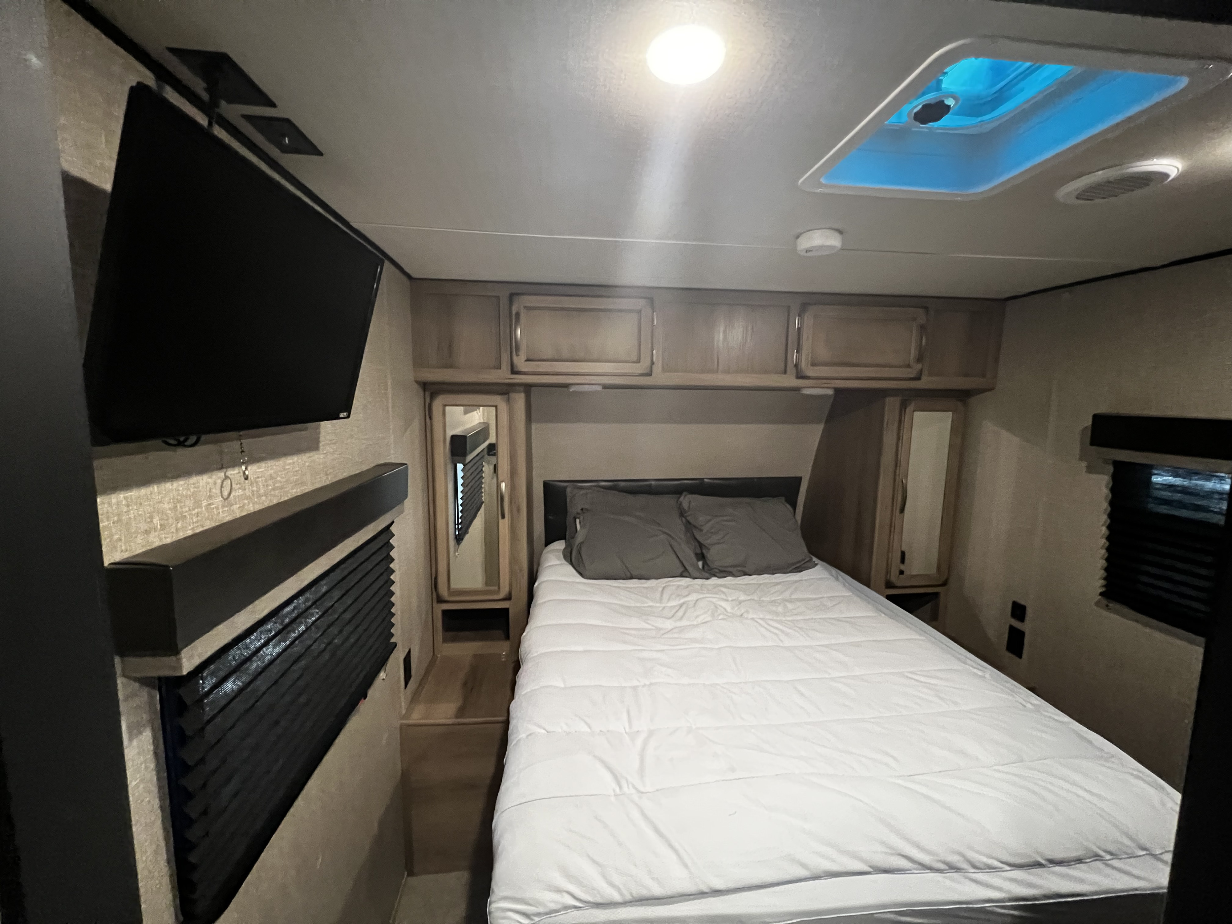 RV rental bedroom: Enjoy a comfortable bed, wall-mounted TV, storage cabinets, and a bright skylight.. Grand Design Transcend 2019