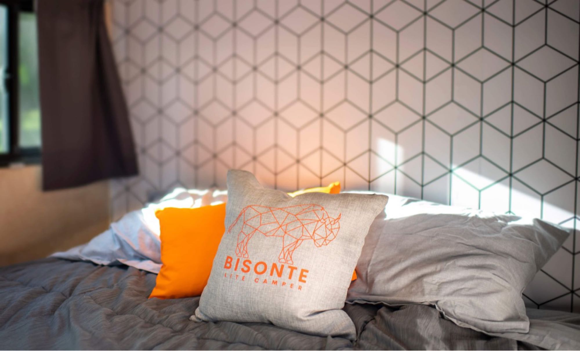 Relaxing RV rental interior: a cozy bed with decorative pillows, one for "Bisonte Lite Camper," and a patterned wall.. Superior Lite Camper Deluxe 2022