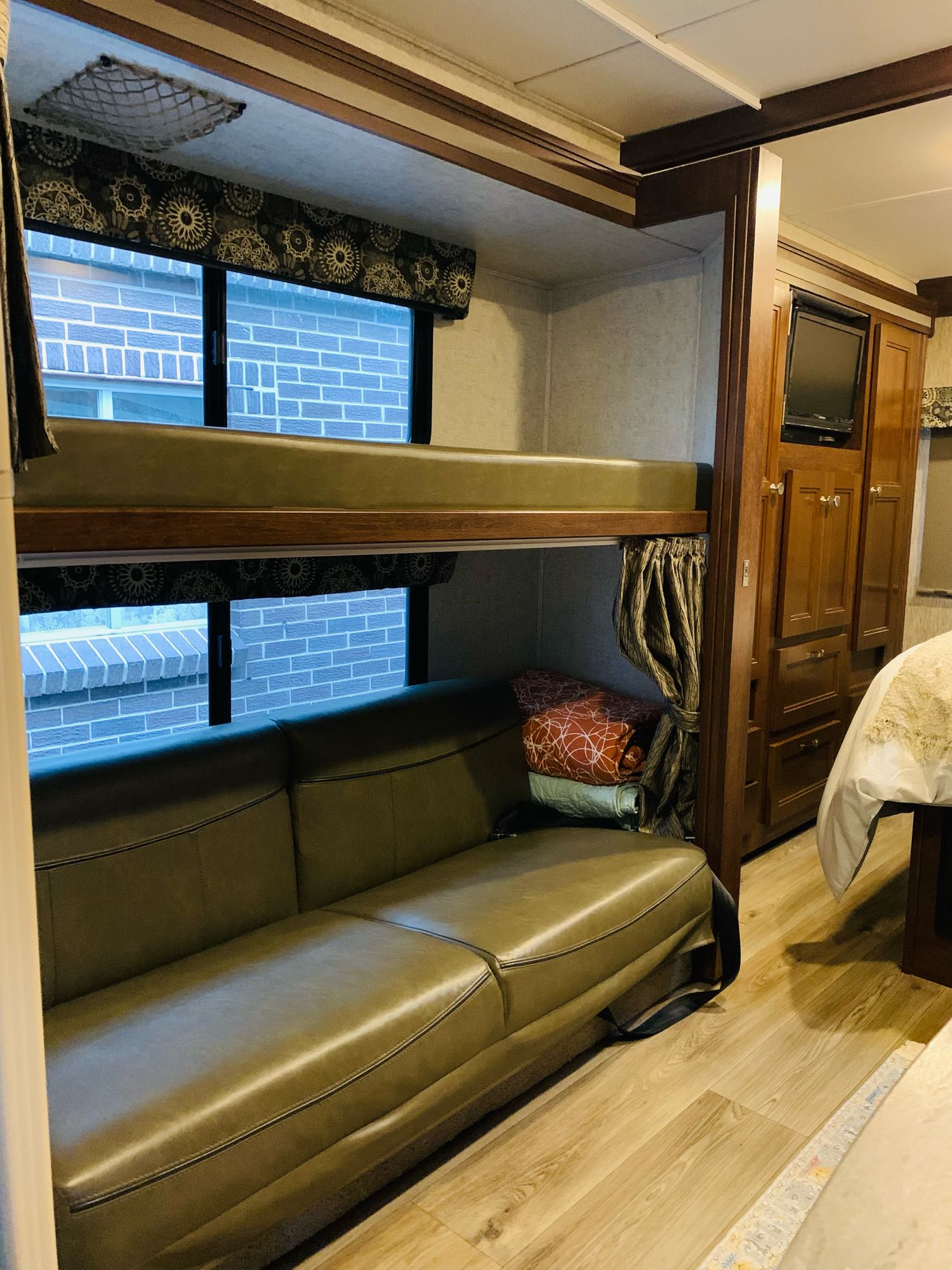 RV rental interior: bunk bed over a green couch, with windows, wooden cabinetry, and a TV creating a compact living space.. Forest River Sunseeker 2017
