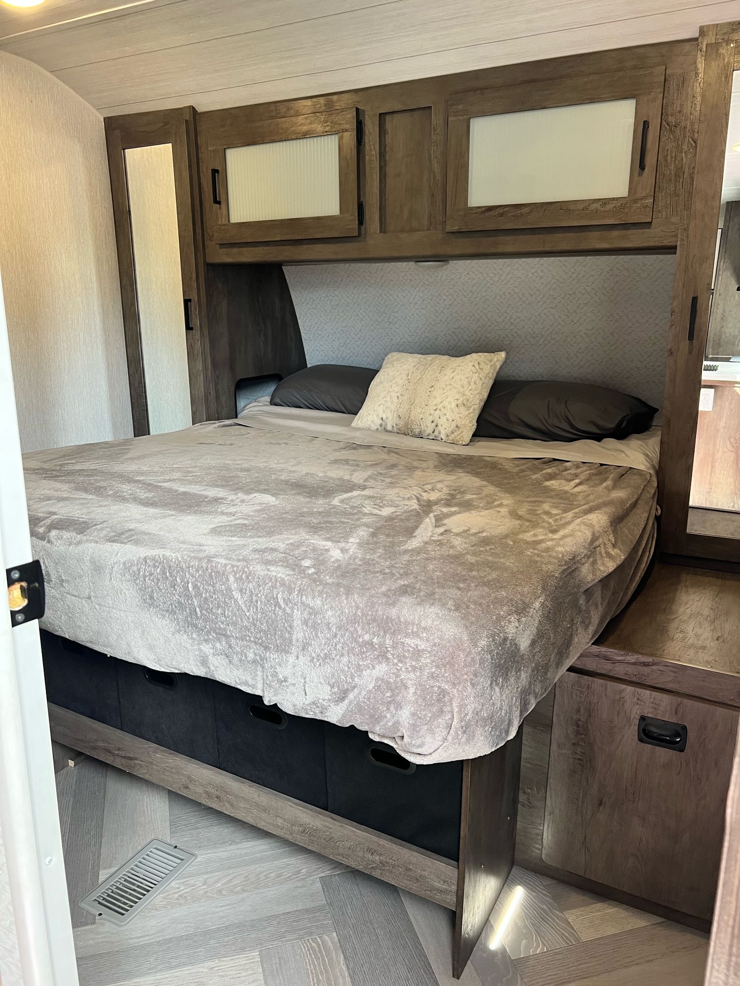 This RV rental bedroom features a bed with gray bedding, overhead cabinets, mirrored wardrobes, and convenient under-bed storage.. Forest River 32BHDS 2022