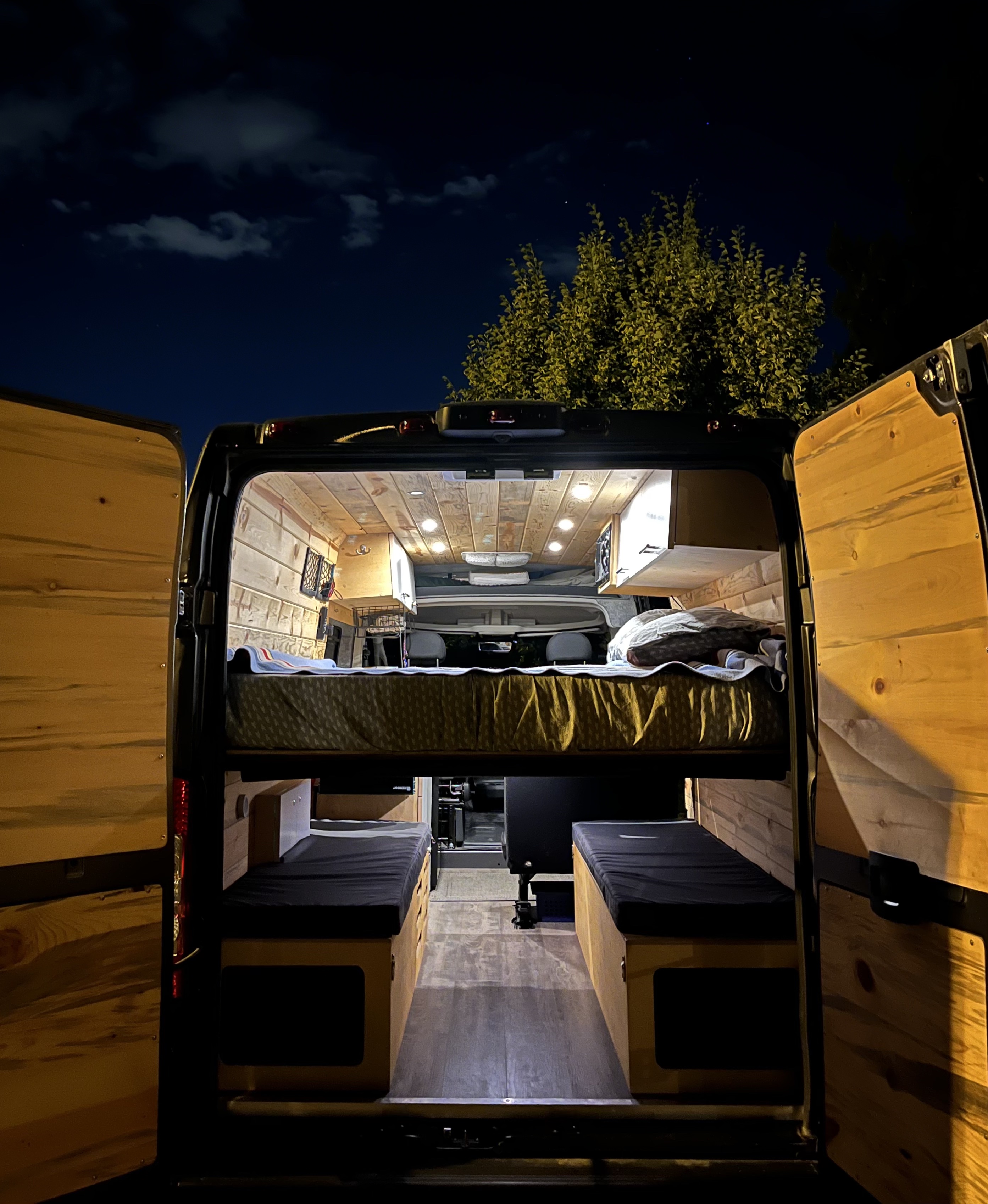 Cozy RV rental camper van interior at night, revealing a custom bunk bed and lower lounge seating.. Dodge Ram Promaster 2500 159 WB 2021