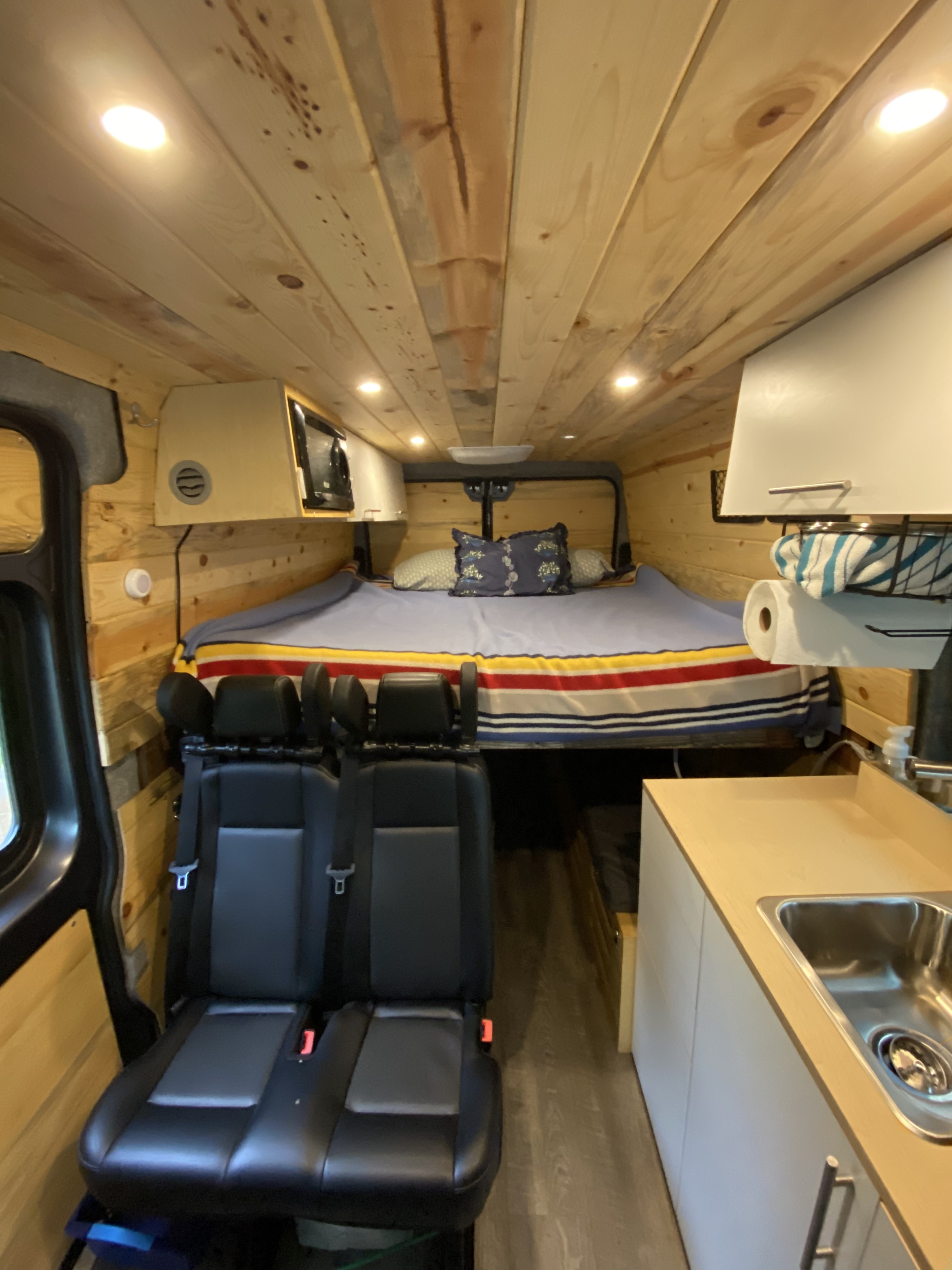 RV rental interior: cozy wood-paneled space with a bed, passenger seats, and compact kitchen—ready for adventure.. Dodge Ram Promaster 2500 159 WB 2021