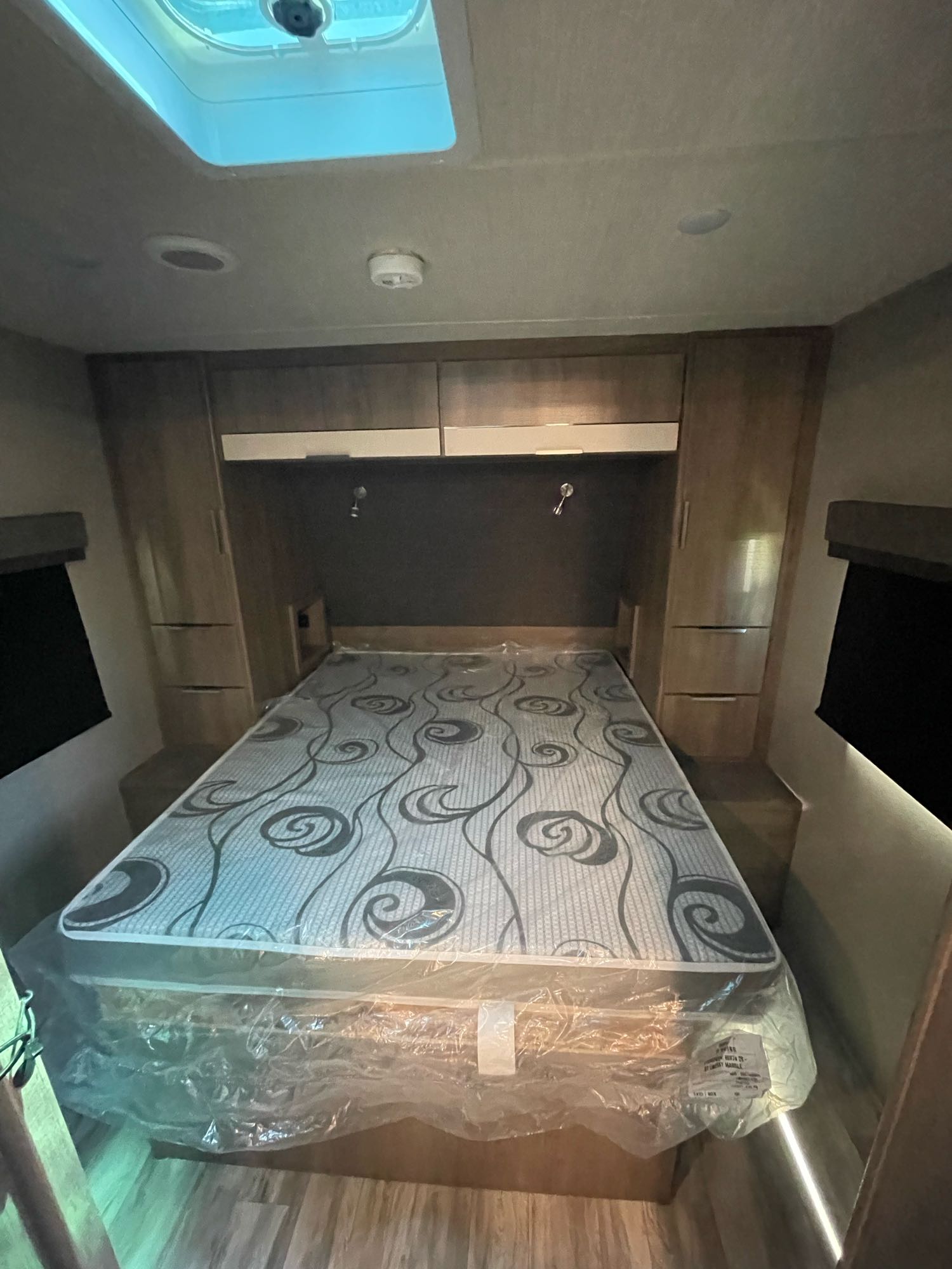 Interior of an RV rental bedroom with a new mattress in plastic, ceiling vent, and built-in storage.. Grand Design Imagine XLS 2021