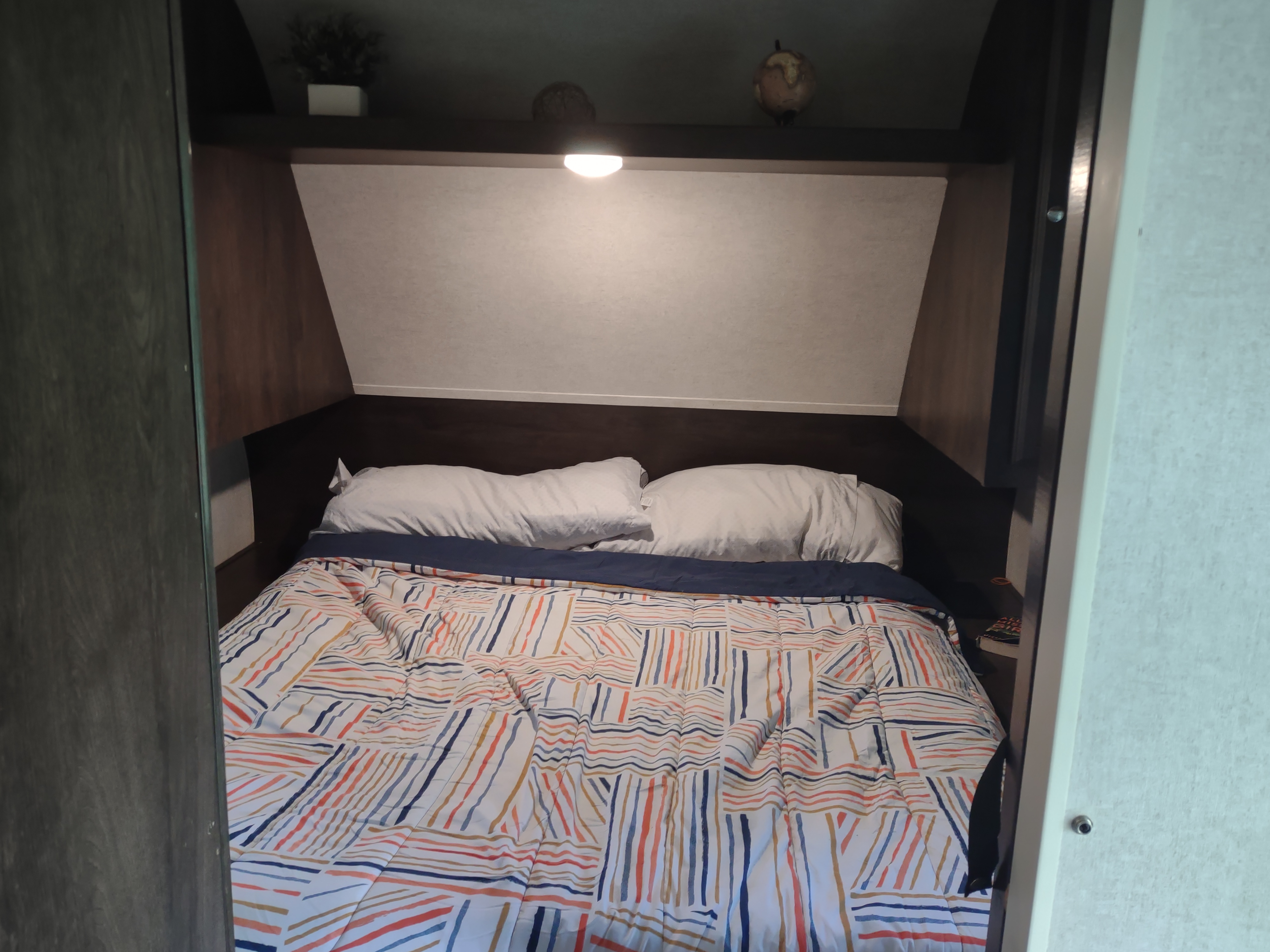 Inside a cozy RV rental bedroom, featuring a striped comforter, white pillows, and a built-in shelf with decor.. Starcraft Autumn Ridge Outfitter 2019