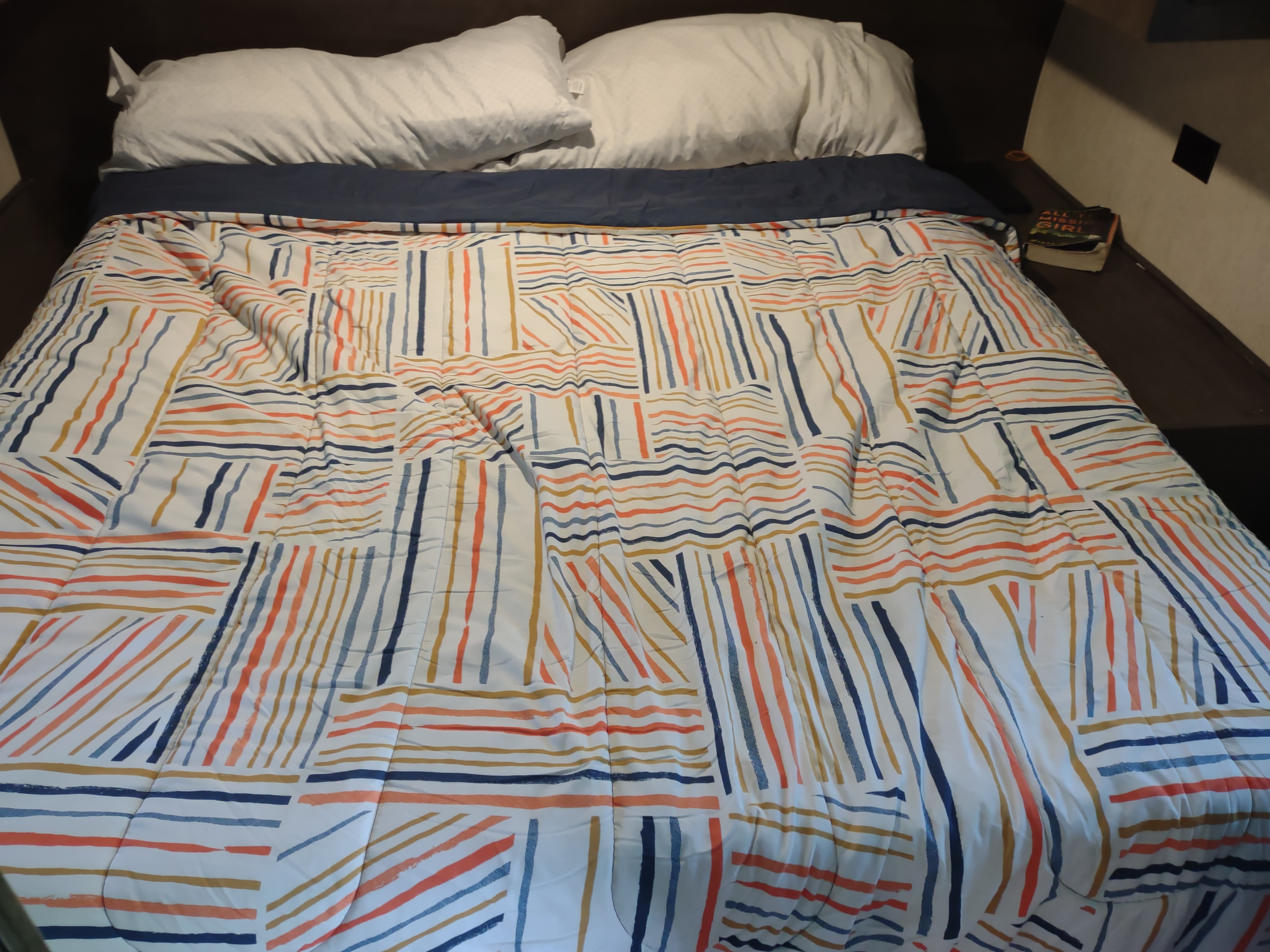 Made bed in an RV rental with white pillows and a white, orange, blue, and gold striped comforter.. Starcraft Autumn Ridge Outfitter 2019