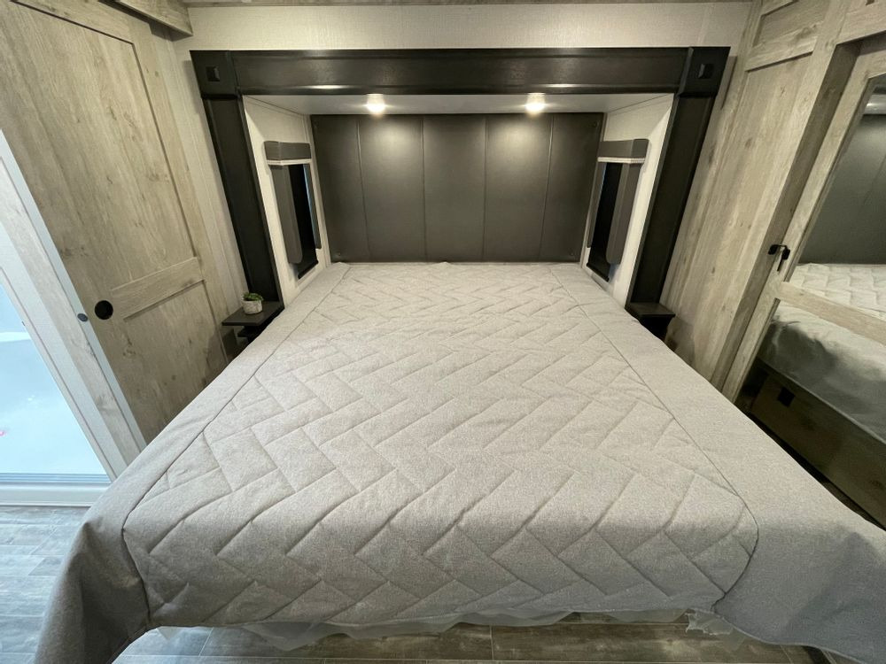 Inside an RV rental bedroom: a comfortable bed with a modern headboard, integrated nightstands, and light wood storage.. Keystone RV Alpine Avalanche 2024
