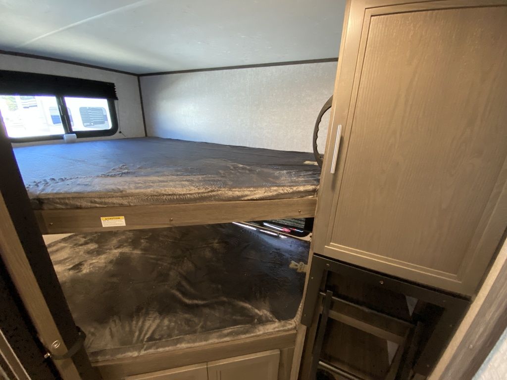 RV rental: Bunk beds with gray blankets & cabinet storage, set in a cozy interior with a window.. Dutchmen Kodiak Ultra Lite 2021
