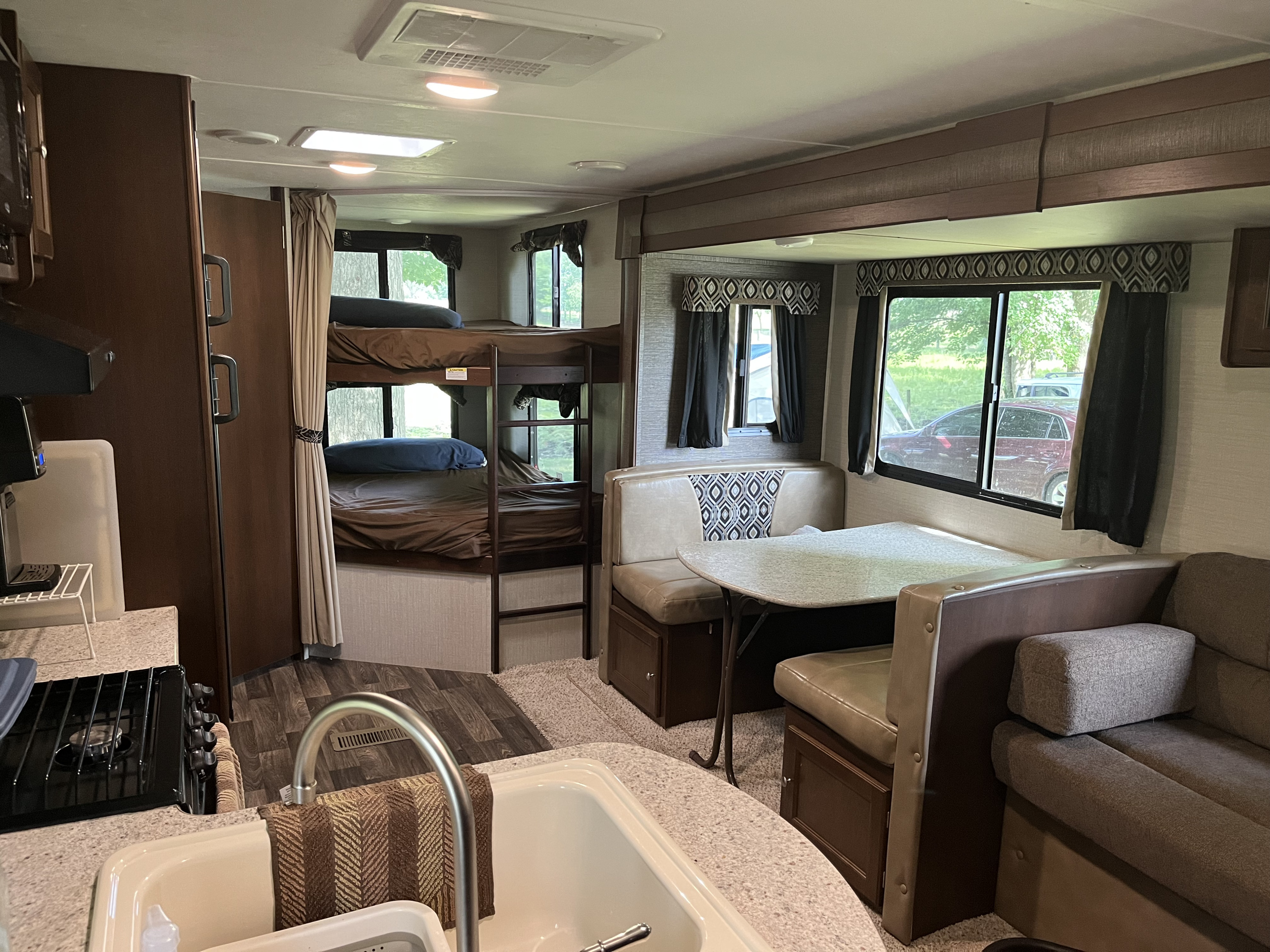 View inside an RV rental showing a kitchen, bunk beds, and dining area with booth seating. Natural light fills the space.. Keystone RV Bullet Ultra Lite 2016