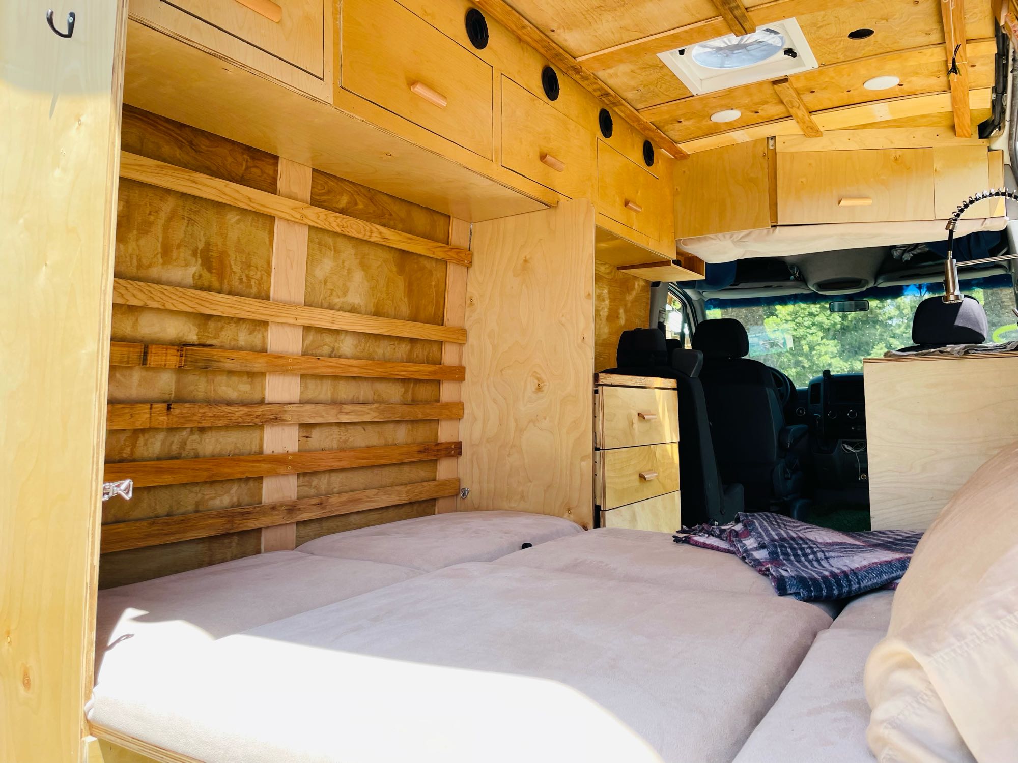 RV rental interior: custom wood camper van with comfortable bed, overhead storage, and built-in drawers for travel.. Dodge Sprinter Van 2007