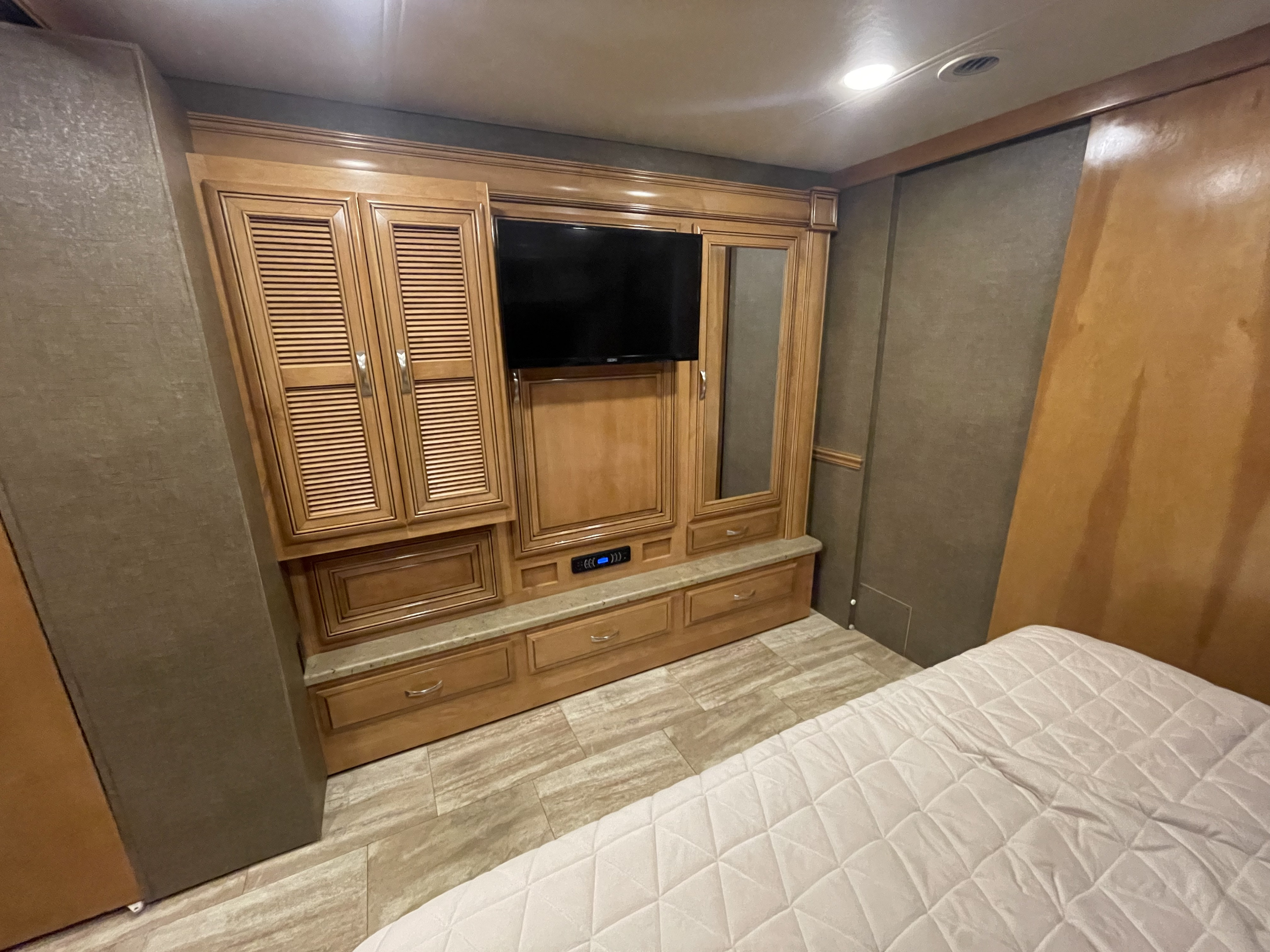 RV rental bedroom interior: a large wooden built-in unit with TV, louvered cabinets, drawers, and a comfortable bed.. Thor Challenger 2017