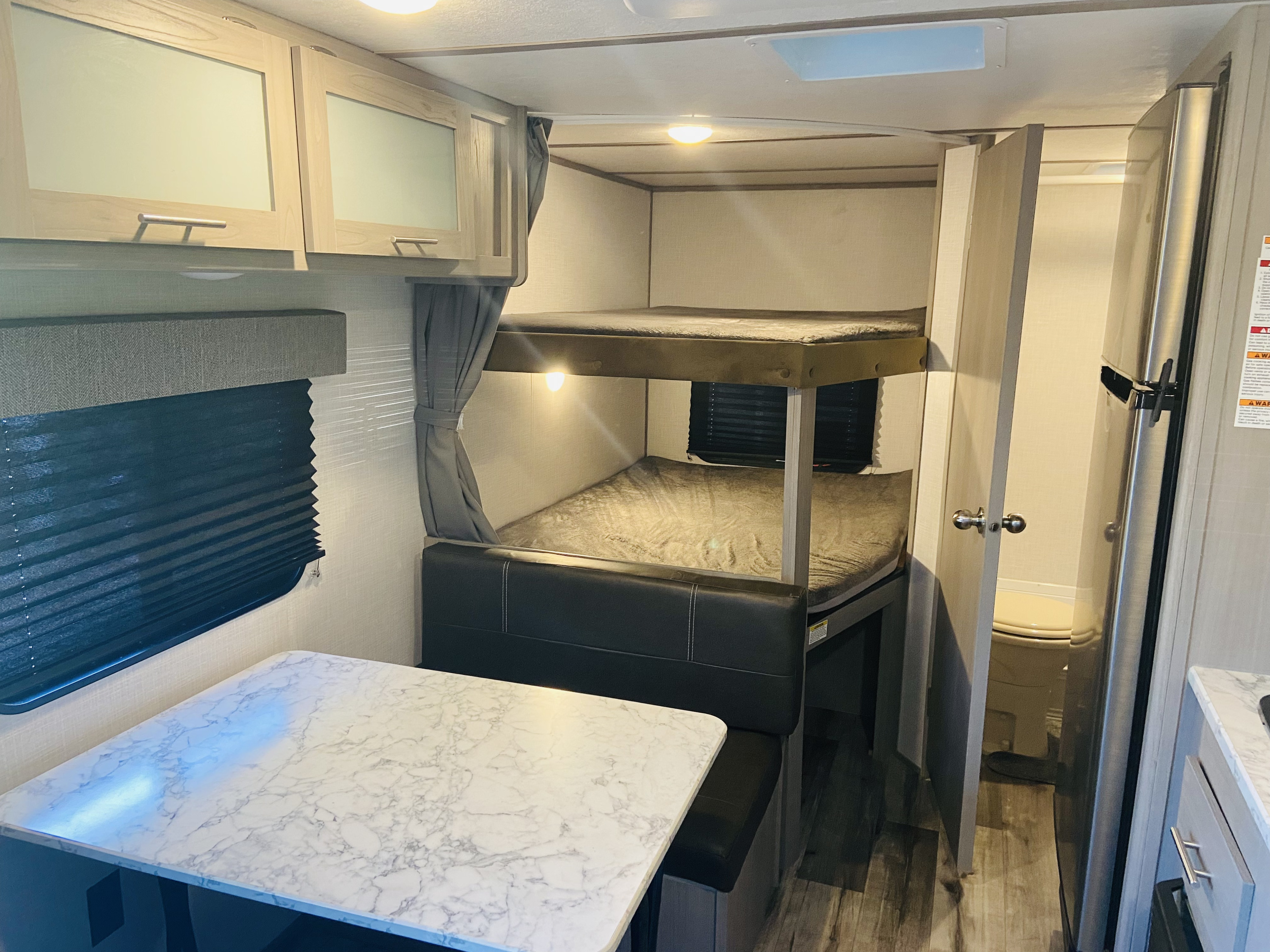 RV rental interior featuring a dinette, double bunk beds with privacy curtains, and a partial view of the bathroom.. Dutchmen bh18 2022