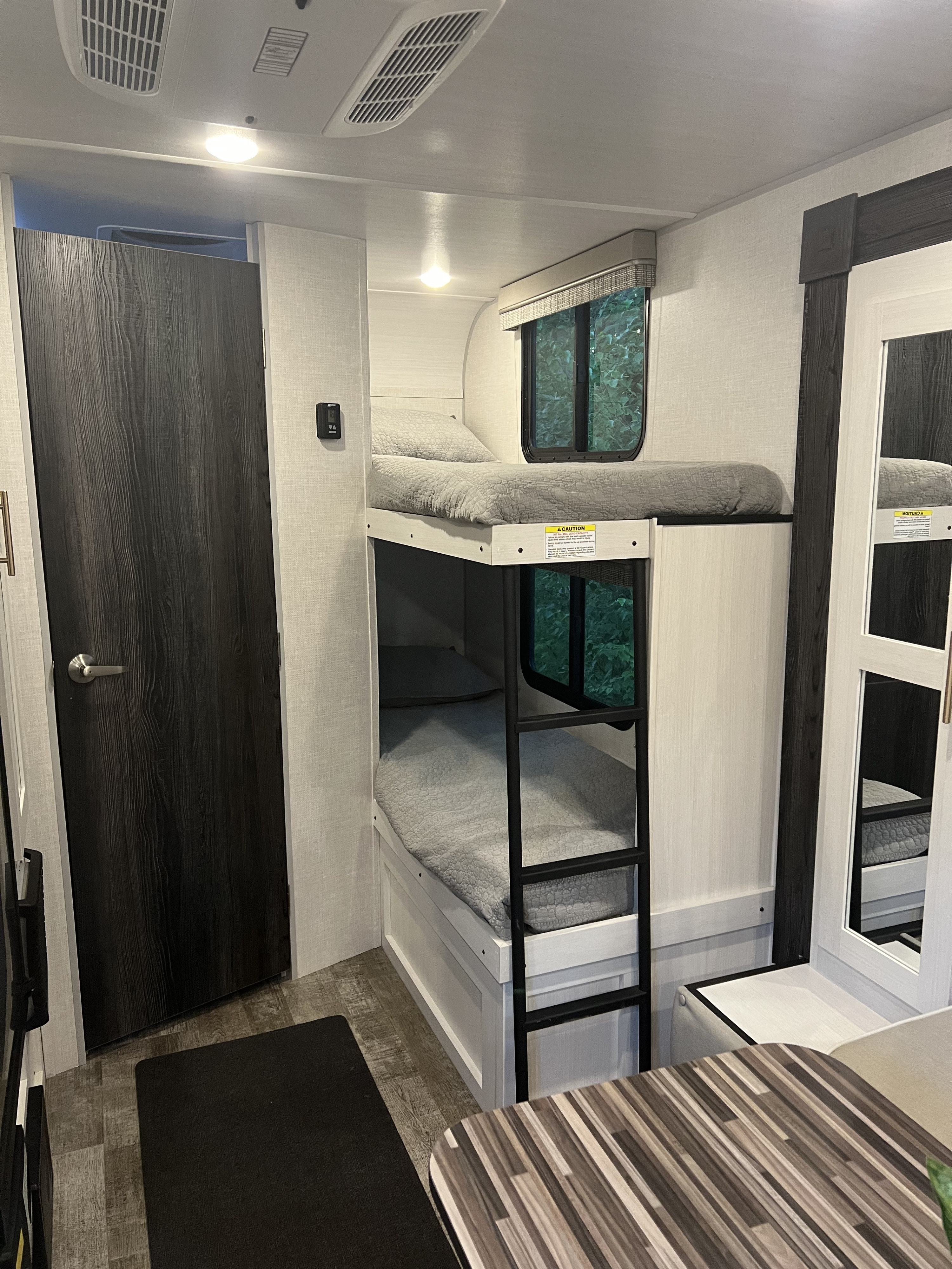 This RV rental shows bunk beds with grey bedding, windows, and a dark door, offering a compact, cozy space.. Forest River R-Pod 193 2022