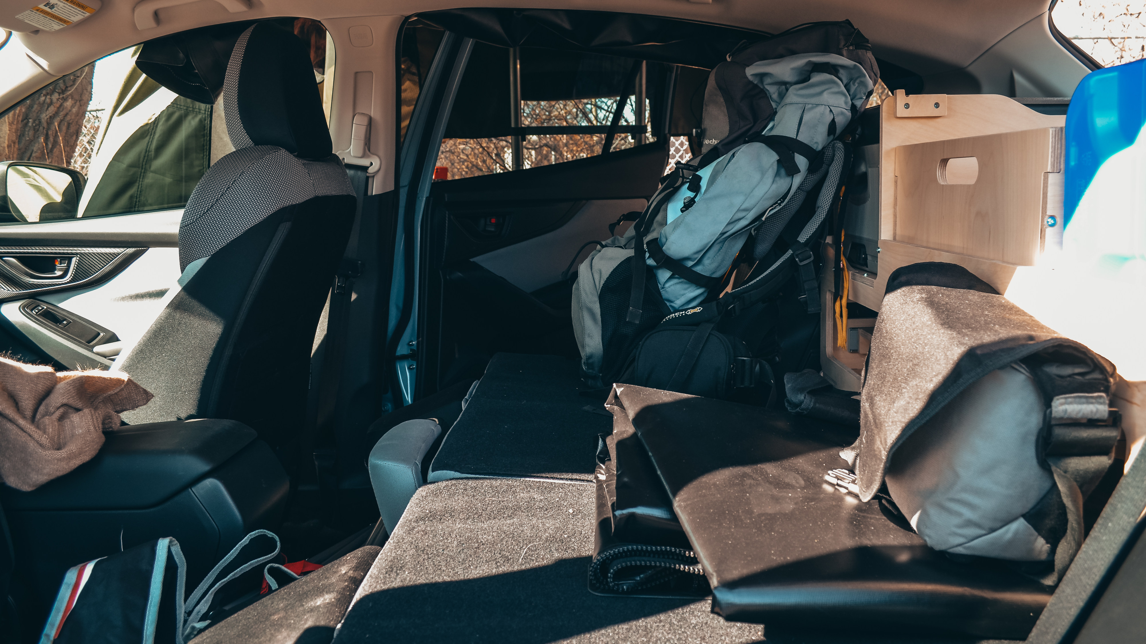 Car interior prepped for adventure: folded seats, custom storage, and backpack. A compact rv rental alternative.. Ford Escape 2025