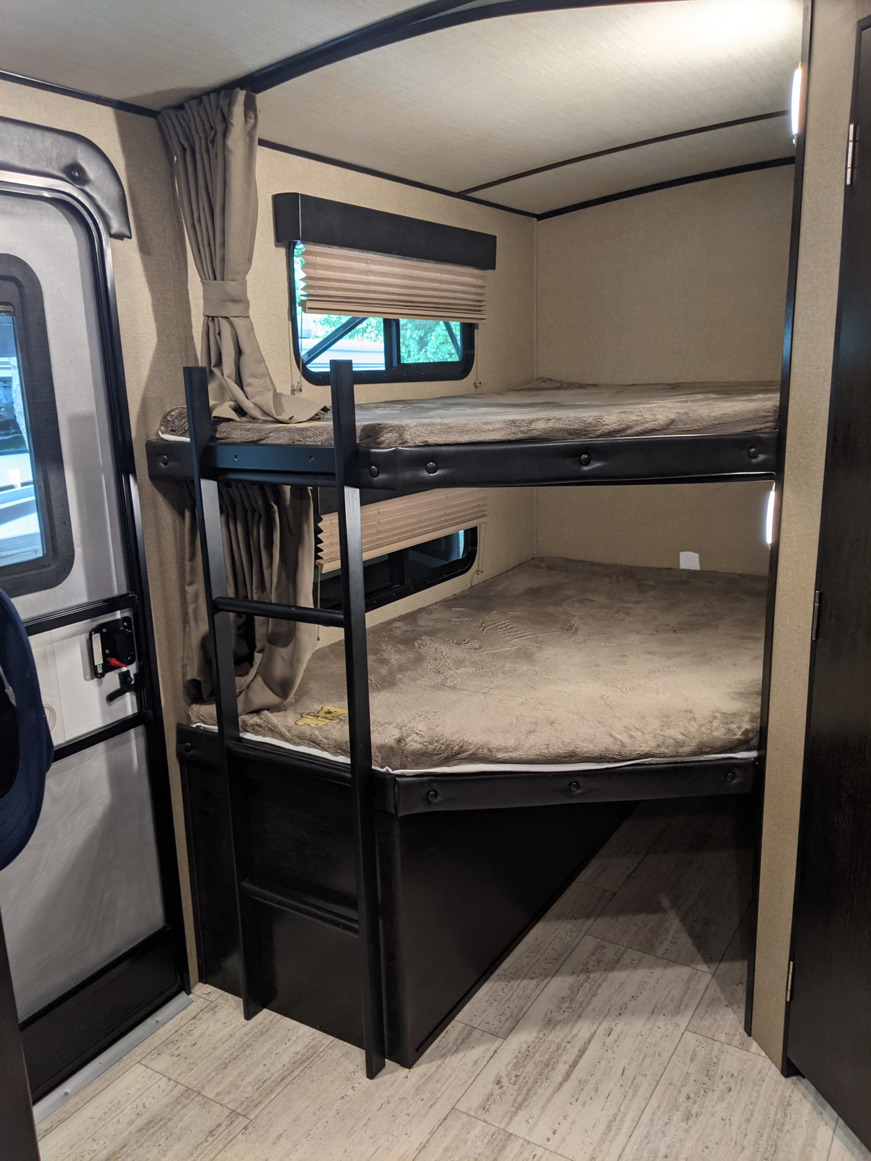 Cozy bunk beds inside an RV rental, featuring two sleeping berths, a ladder, windows with blinds, and light wood-look flooring.. Grand Design Imagine 2019