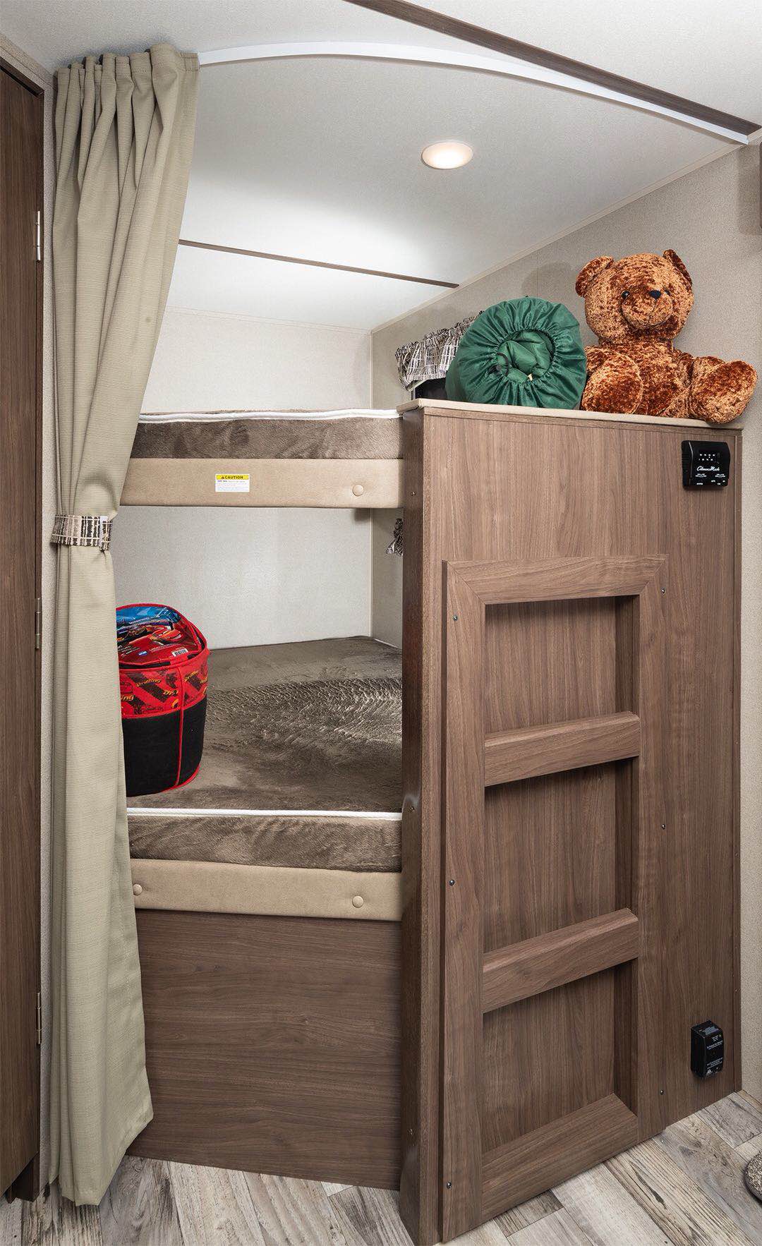 RV rental bunk beds featuring a privacy curtain, fold-down ladder, and cozy mattresses. A teddy bear sits above.. Keystone RV Hideout LHS 2019
