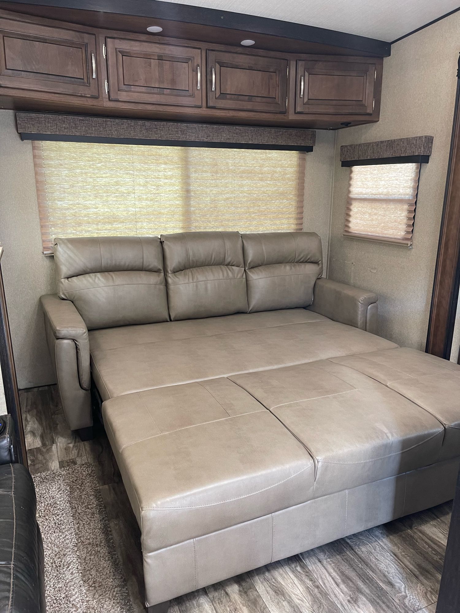 Spacious RV rental interior featuring a pulled-out tan sofa bed, dark wood overhead cabinets, and window blinds. Ideal for comfort.. Grand Design Reflection 2020