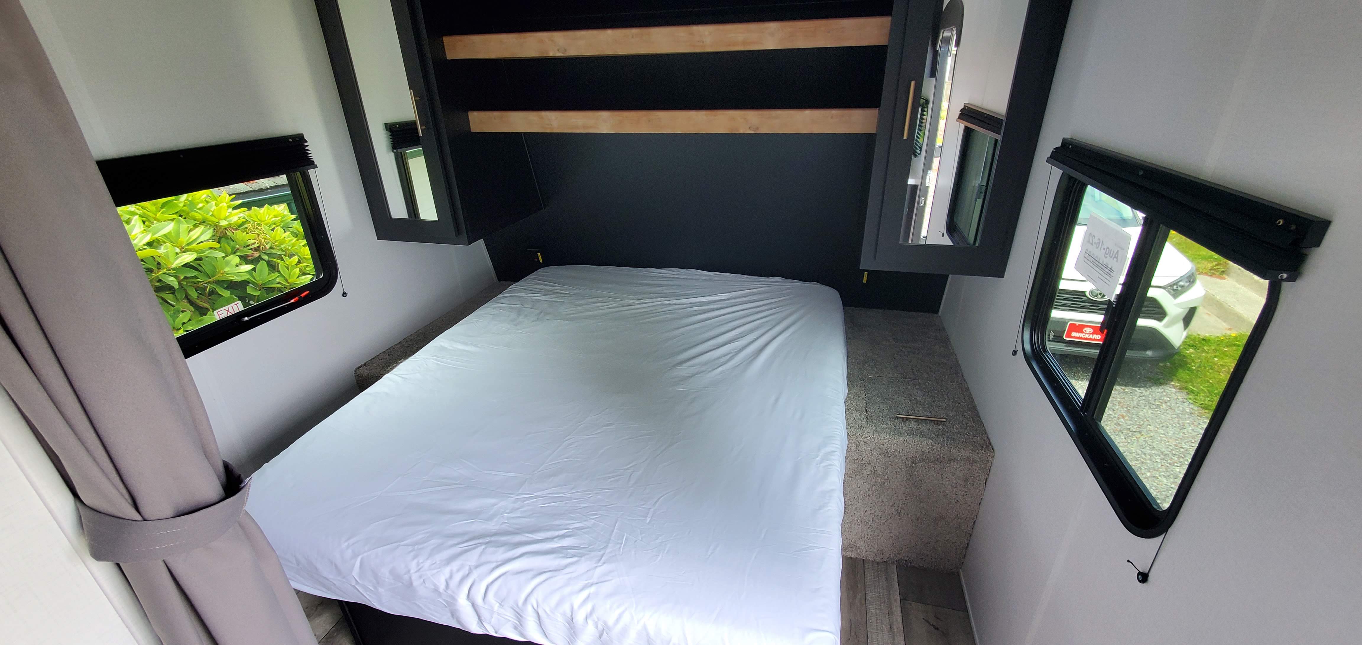 Comfortable RV rental bedroom featuring a modern dark headboard, white bed, side windows, and overhead storage.. Keystone RV Springdale 2022