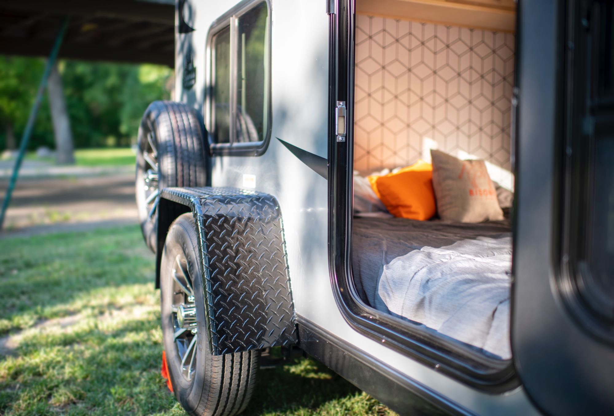 Close-up of a compact RV rental camper parked on grass, door open revealing a comfortable bed & modern patterned interior.. Superior Lite Camper Deluxe 2022