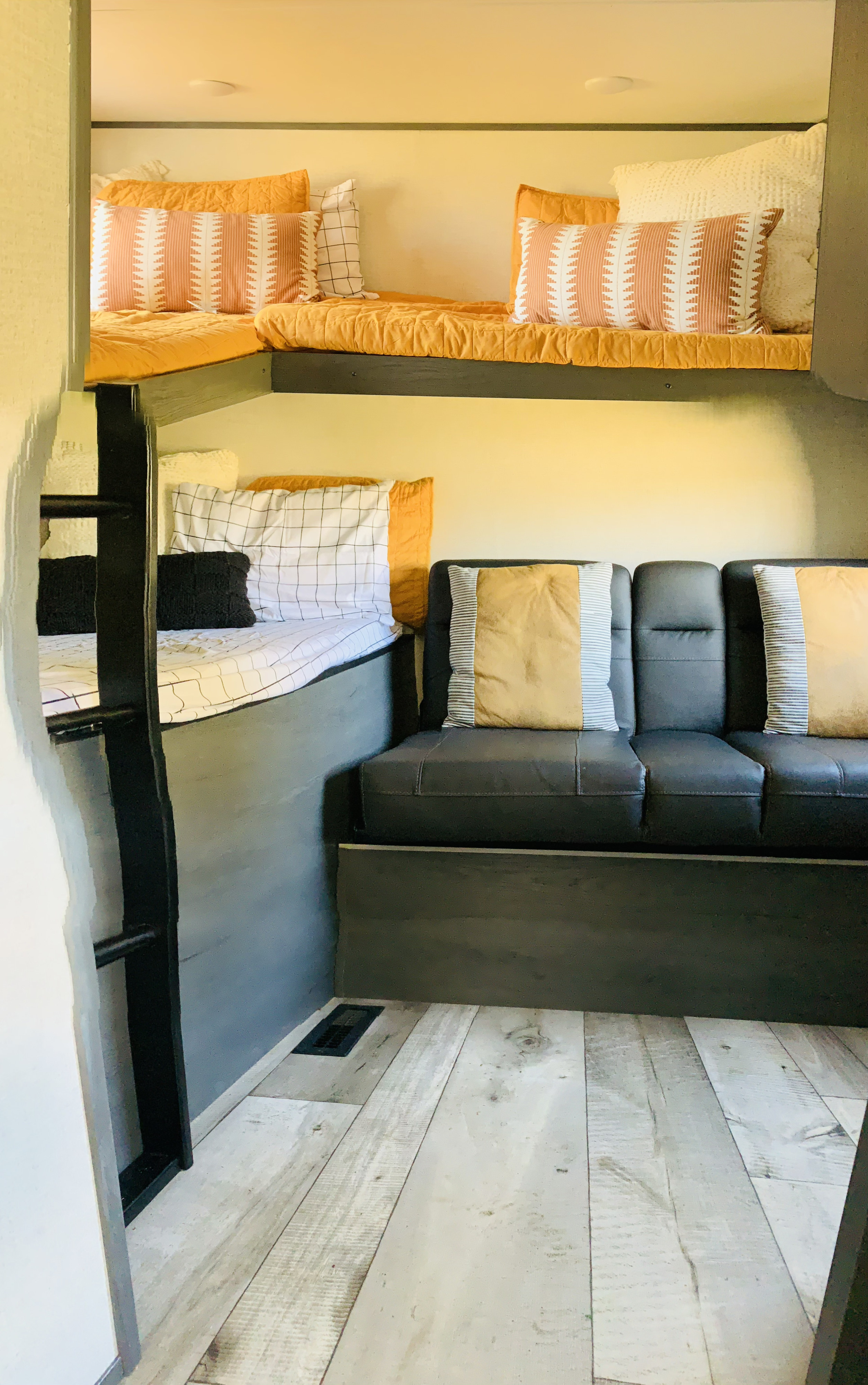 Cozy RV rental interior with bunk beds, ladder, and sofa. Warm-toned bedding and light wood floor create a welcoming space.. Dutchmen Aspen Trail 2022