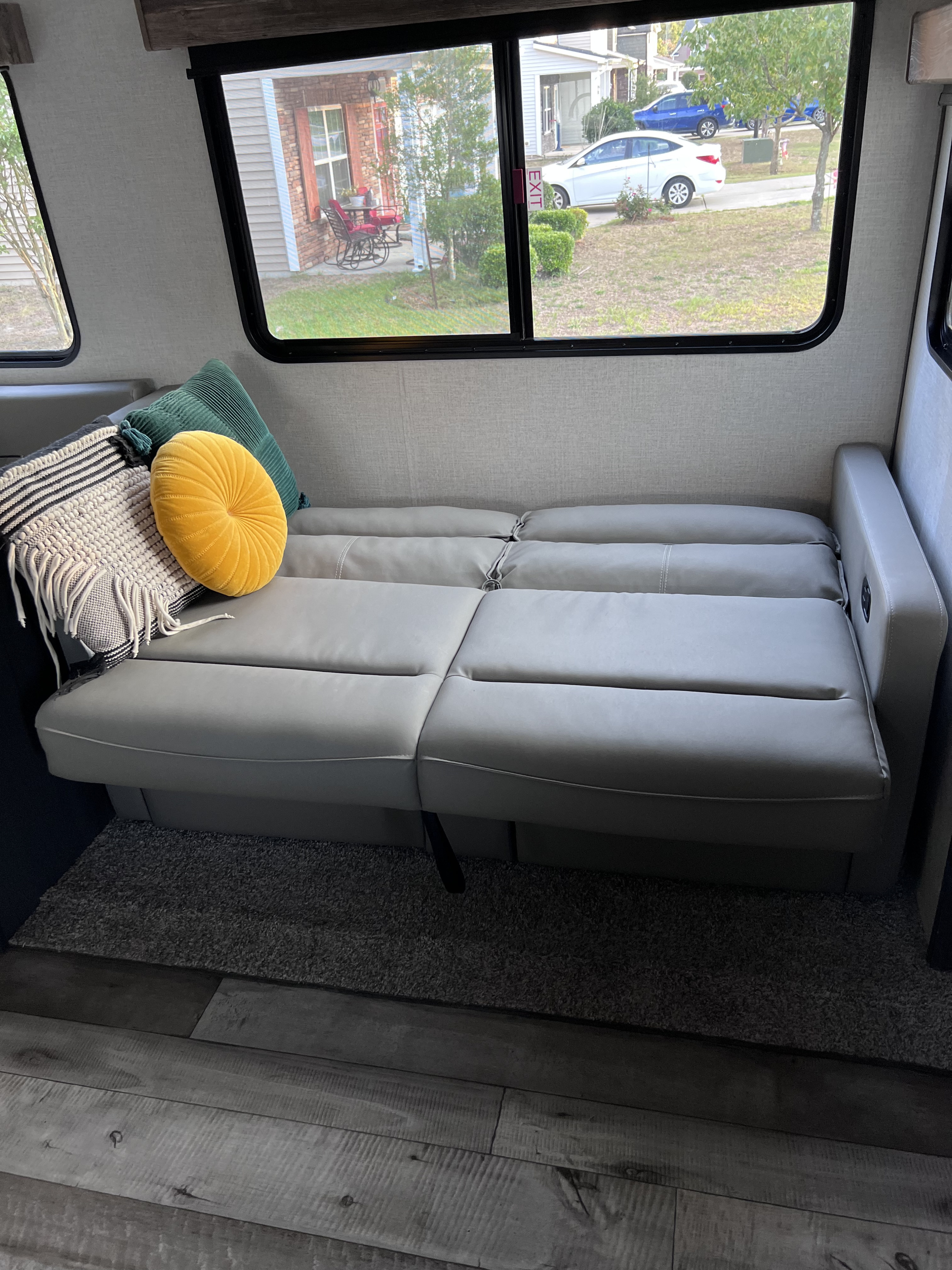 Inside an RV rental: versatile gray sofa converts to a bed, with cozy pillows and a view outside.. Dutchmen Aspen Trail 2022