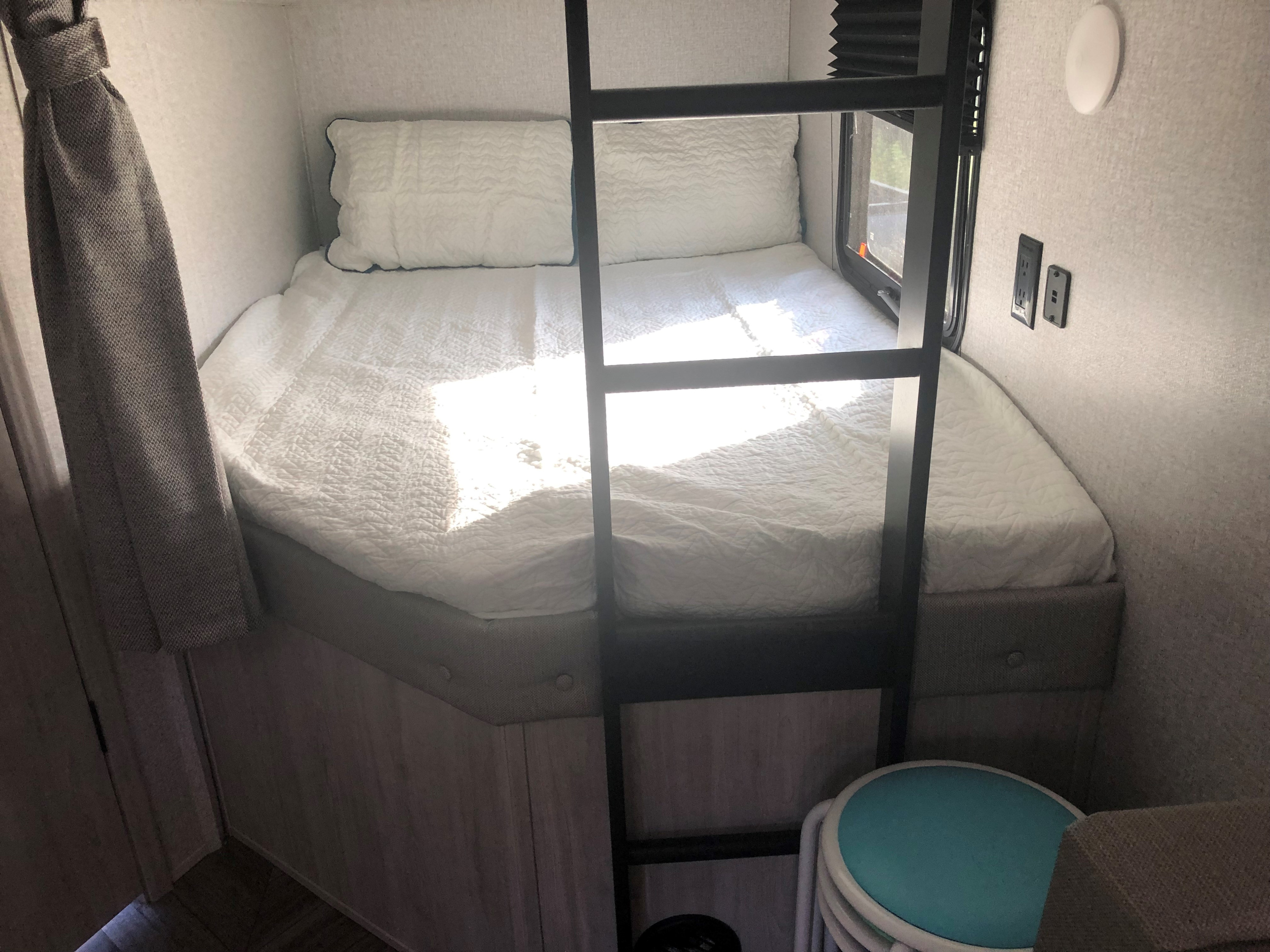 An RV rental interior features a tidy bunk bed with a ladder, window, and wall outlets.. East to West Della Terra 2022