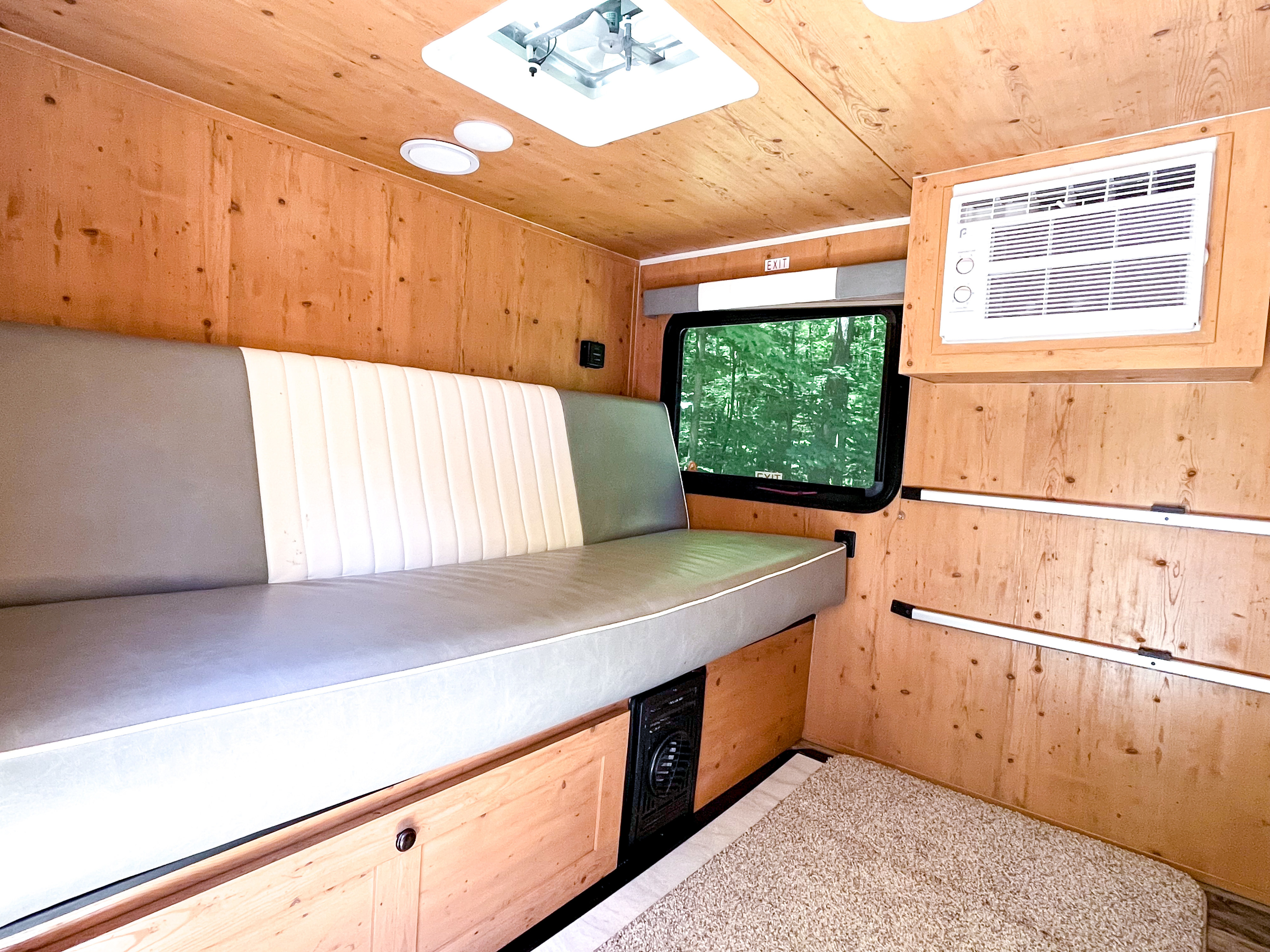 Inside a cozy **RV rental**: wood-paneled walls/ceiling, bench bed, AC unit, window with forest view, and carpeted floor.. Sunset Park and RV 2021 Sunray 115 (similar to Sunray 109) 2021