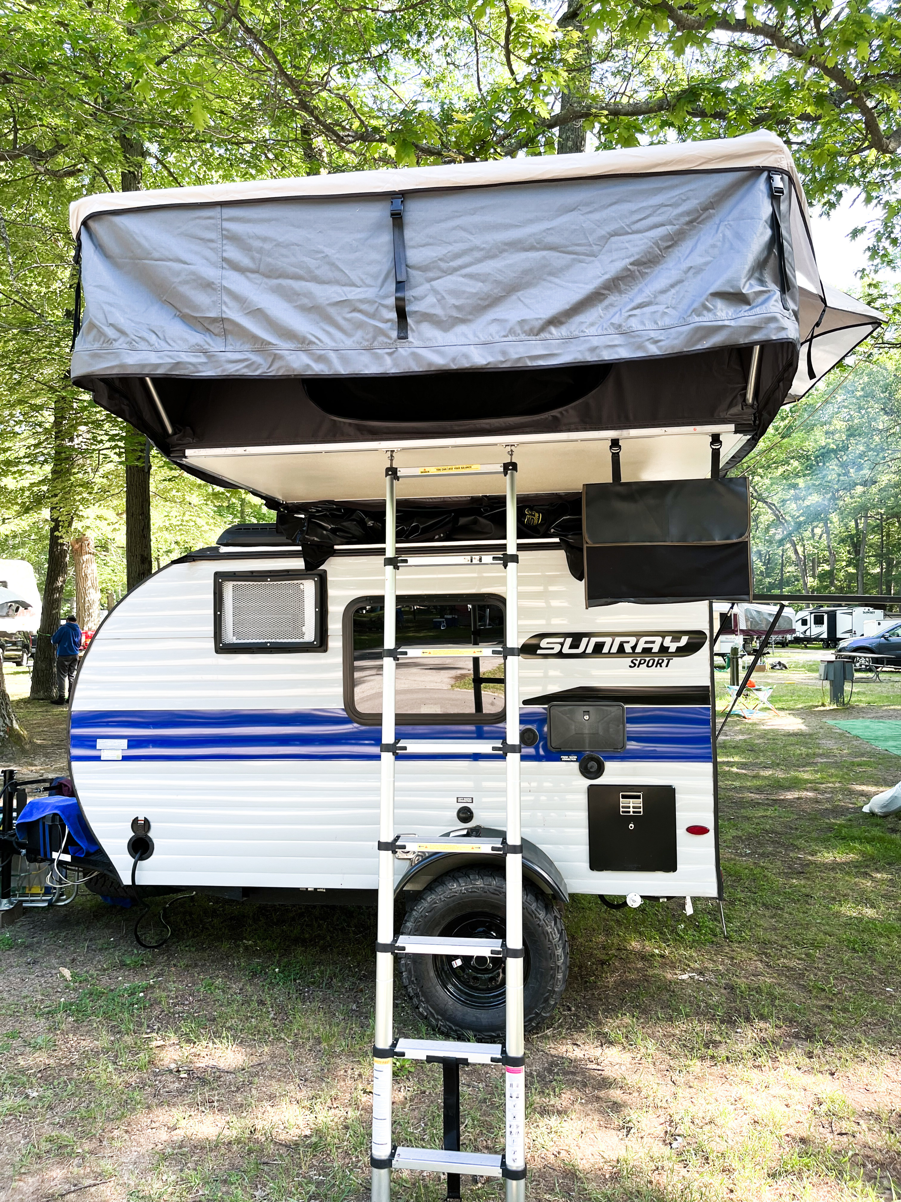 Small white and blue Sunray Sport camper with rooftop tent and ladder, great for an rv rental camping adventure.. Sunset Park and RV 2021 Sunray 115 (similar to Sunray 109) 2021