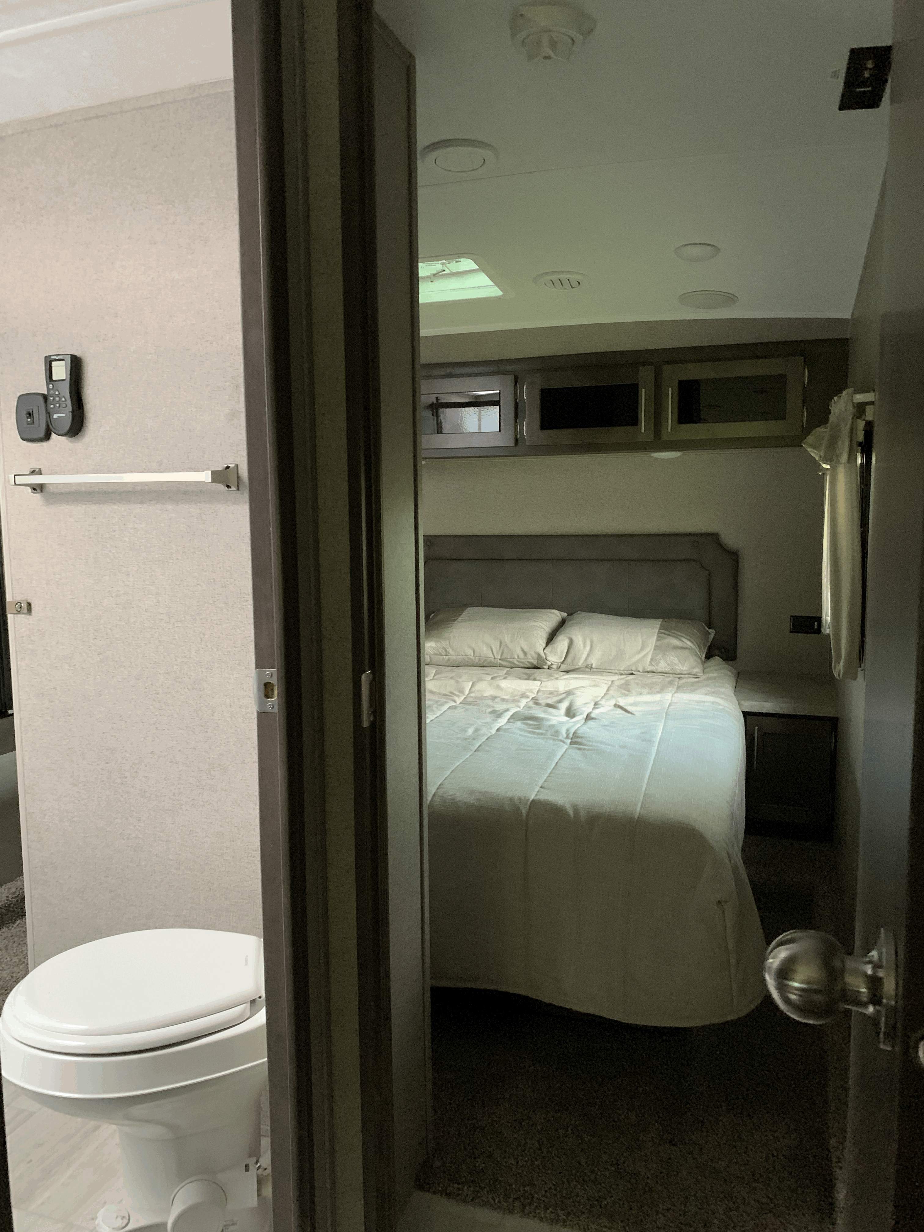 Cozy RV rental interior: bedroom with queen bed, overhead cabinets, and adjacent compact bathroom with toilet.. Forest River Flagstaff Super Lite 2020
