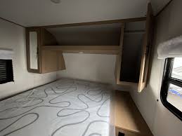 Compact RV rental bedroom with a bed, overhead cabinets, and practical storage solutions.. Avenger LE 2022
