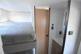 An RV rental's compact interior, featuring a raised bunk bed on the left, with a small vanity and door on the right.. Avenger LE 2022