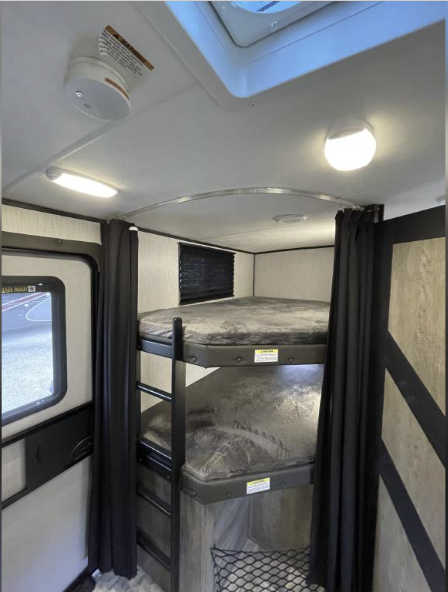RV rental bunk bed area with privacy curtains, safety smoke detector, and bright interior lighting.. Heartland RVs North Trail 2021