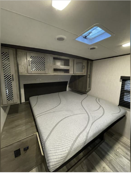 Spacious RV rental bedroom featuring a comfortable bed, ample overhead storage, skylight, and power outlets for travelers.. Heartland RVs North Trail 2021