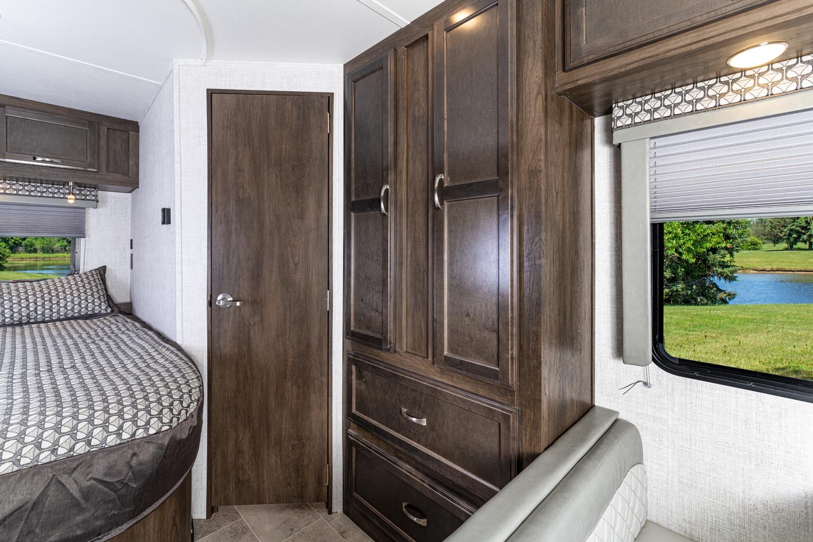 Inside an RV rental: cozy bedroom area with a bed, wooden wardrobe, and window overlooking a lake.. Gulf Stream Conquest 2022