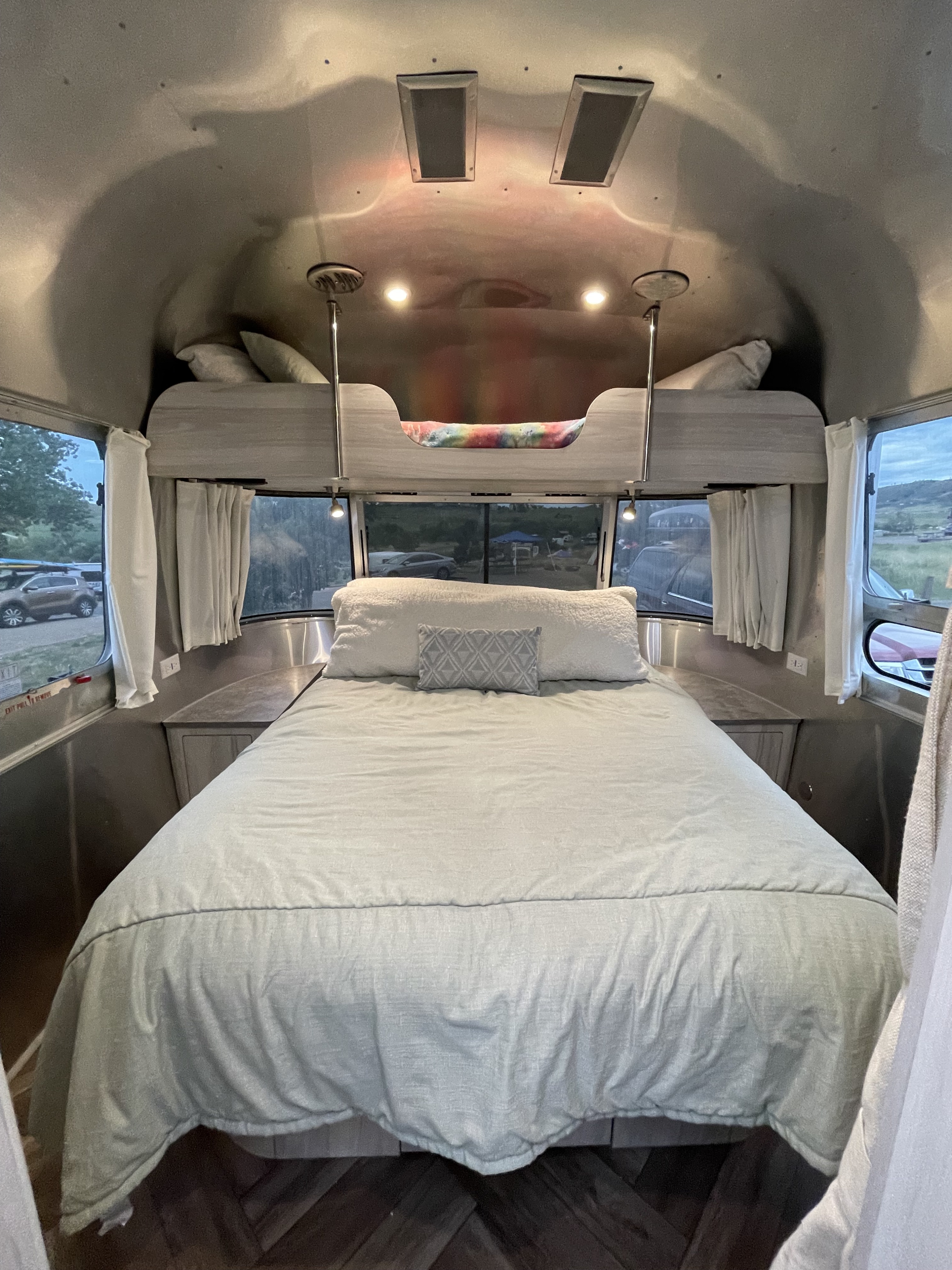 Inside a comfy Airstream RV rental bedroom: main bed below, small bunk above, with views out to the campsite.. Airstream International 2021