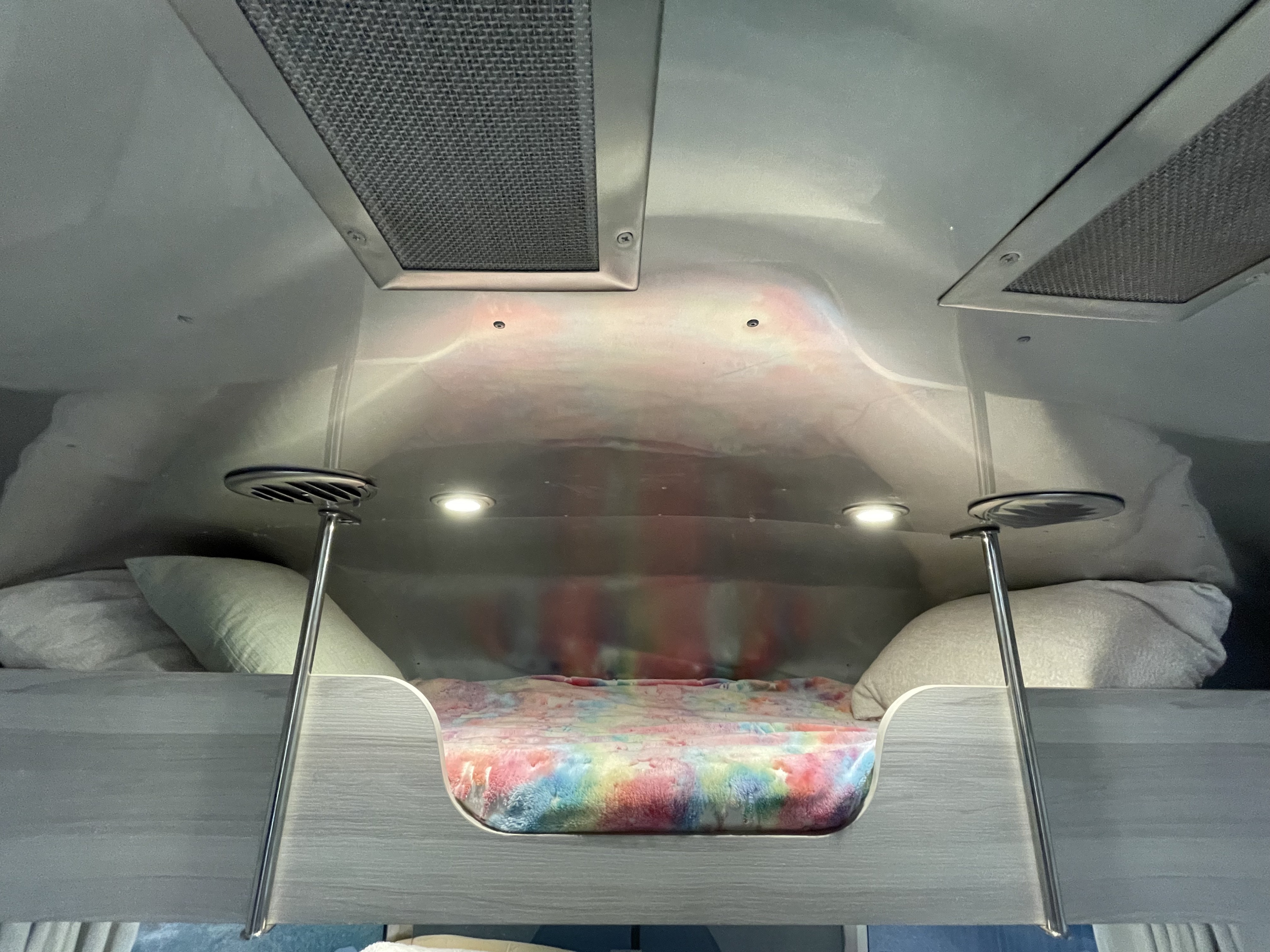 Cozy bunk bed with colorful blanket in an RV rental, featuring overhead vents, bright lights, and sleek bed poles.. Airstream International 2021