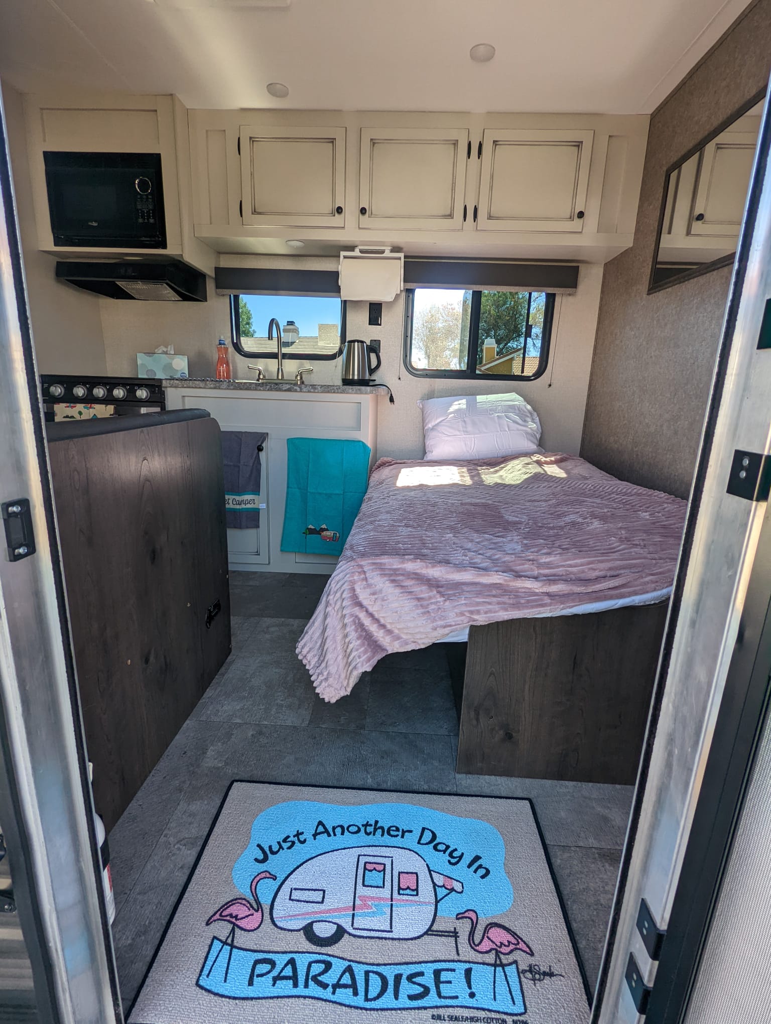 Cozy RV rental interior showing a compact kitchenette, comfortable bed, and a cheerful 'Paradise' floor mat, ideal for camping.. Highland Ridge RV Open Range 2021
