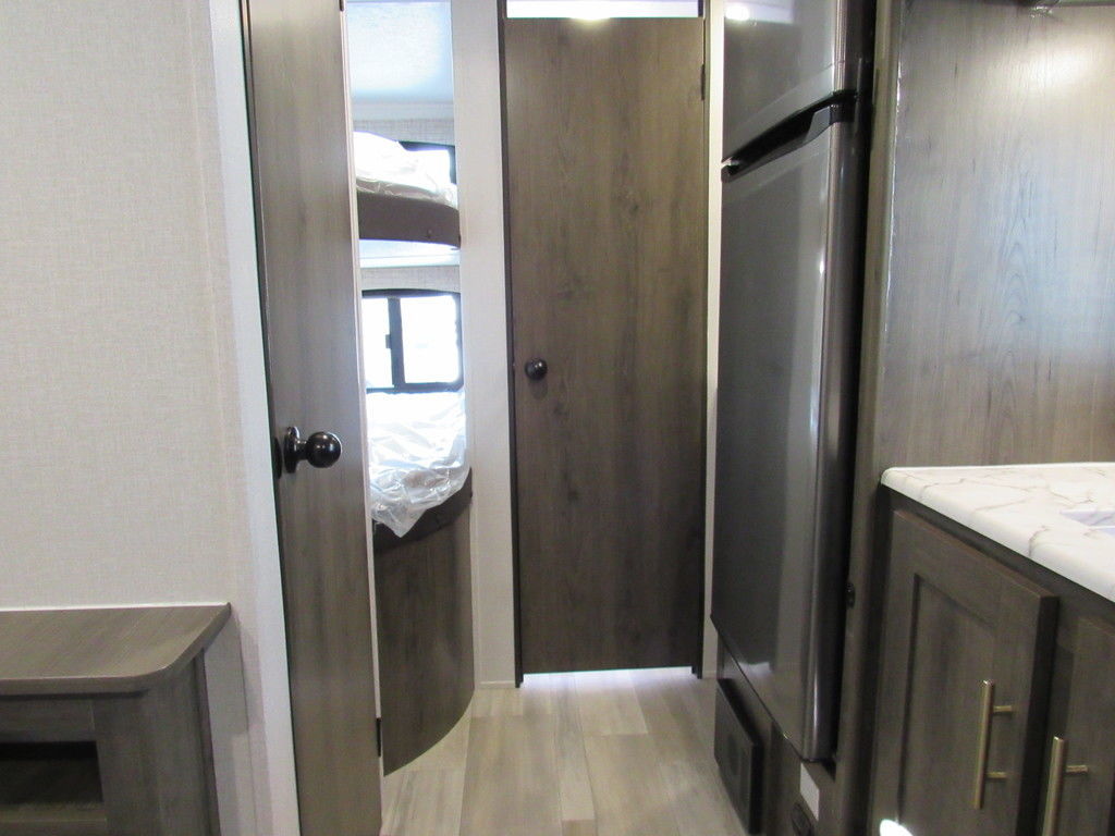 RV rental interior: doorway to bunk beds, closed door, and modern kitchen with a refrigerator. Practical camper layout.. Coachmen Viking 2021