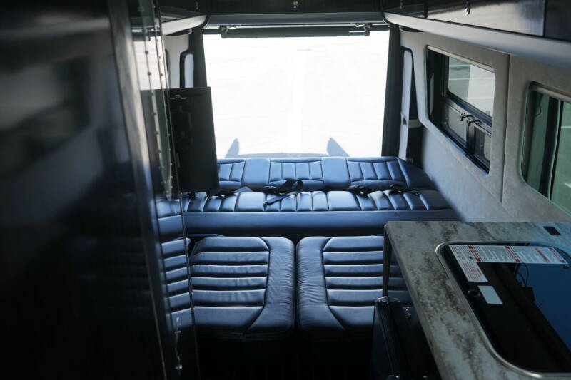 Spacious RV rental interior with black leather seating that converts to a bed, a kitchenette, and mounted TV, ideal for travel.. Airstream Interstate 2016