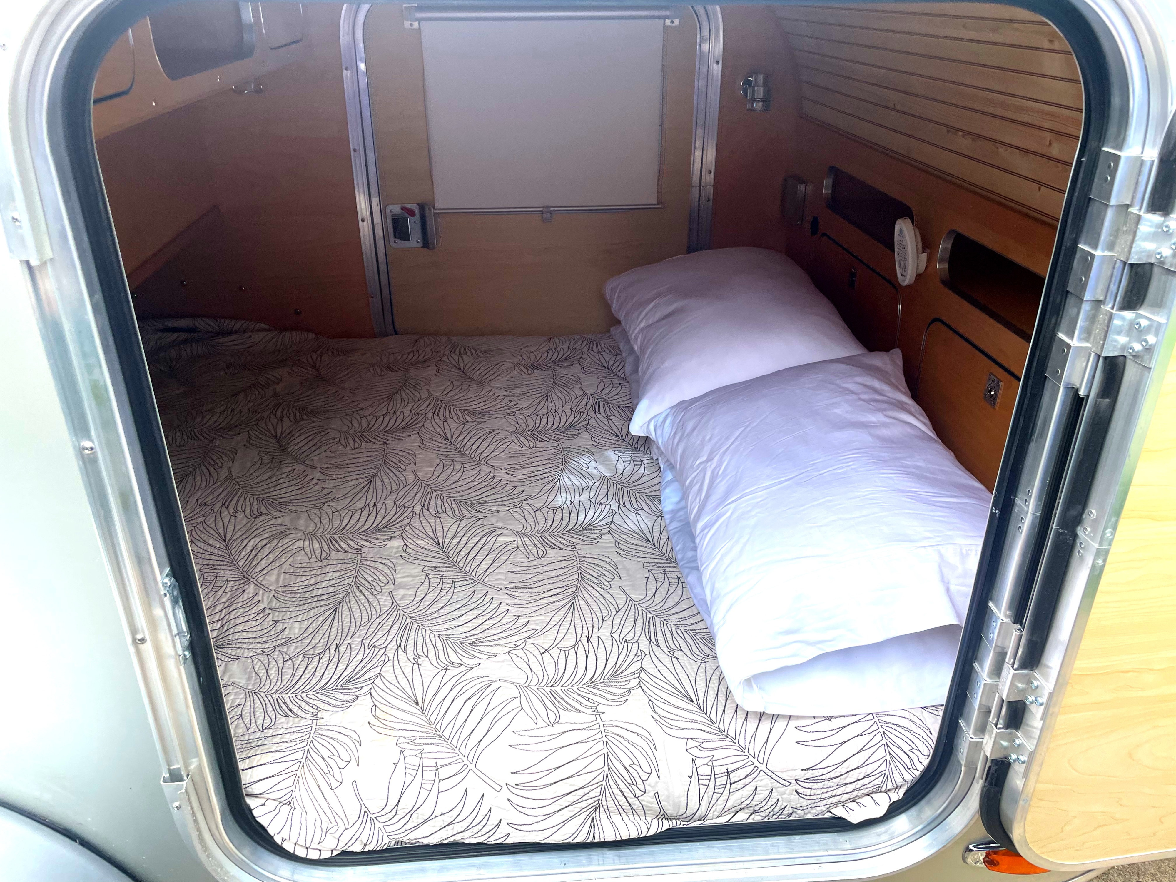 Step inside this cozy rv rental's bedroom, featuring a patterned bedspread, pillows, and warm wood walls.. Other Other 2019