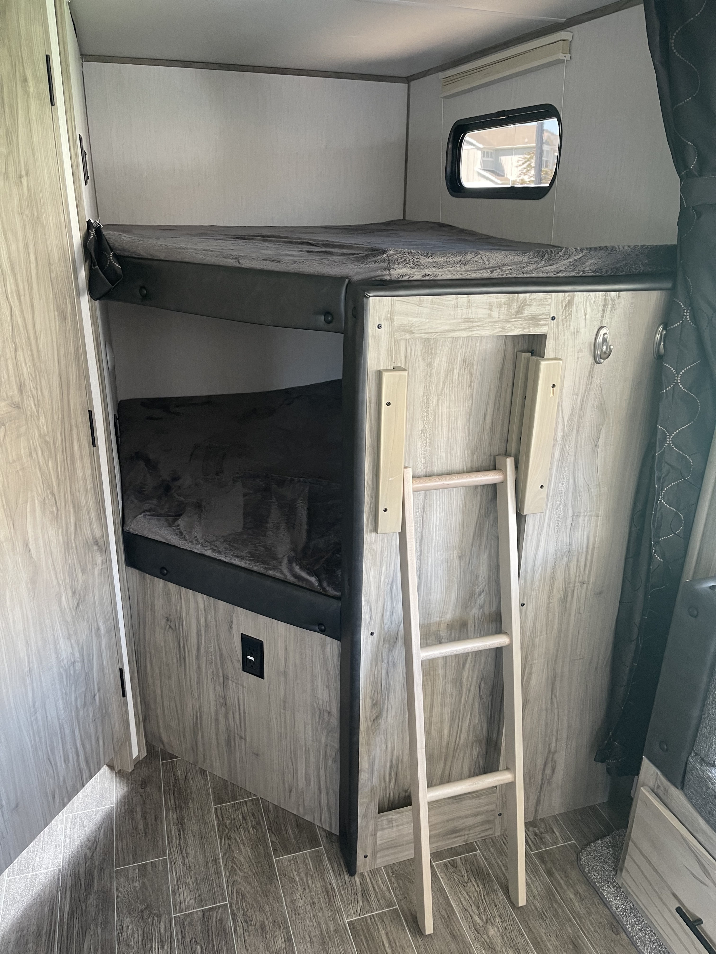 RV rental interior with two cozy bunk beds and a ladder for top bunk access, featuring light wood-grain finishes.. Forest River Cherokee Alpha Wolf 2021