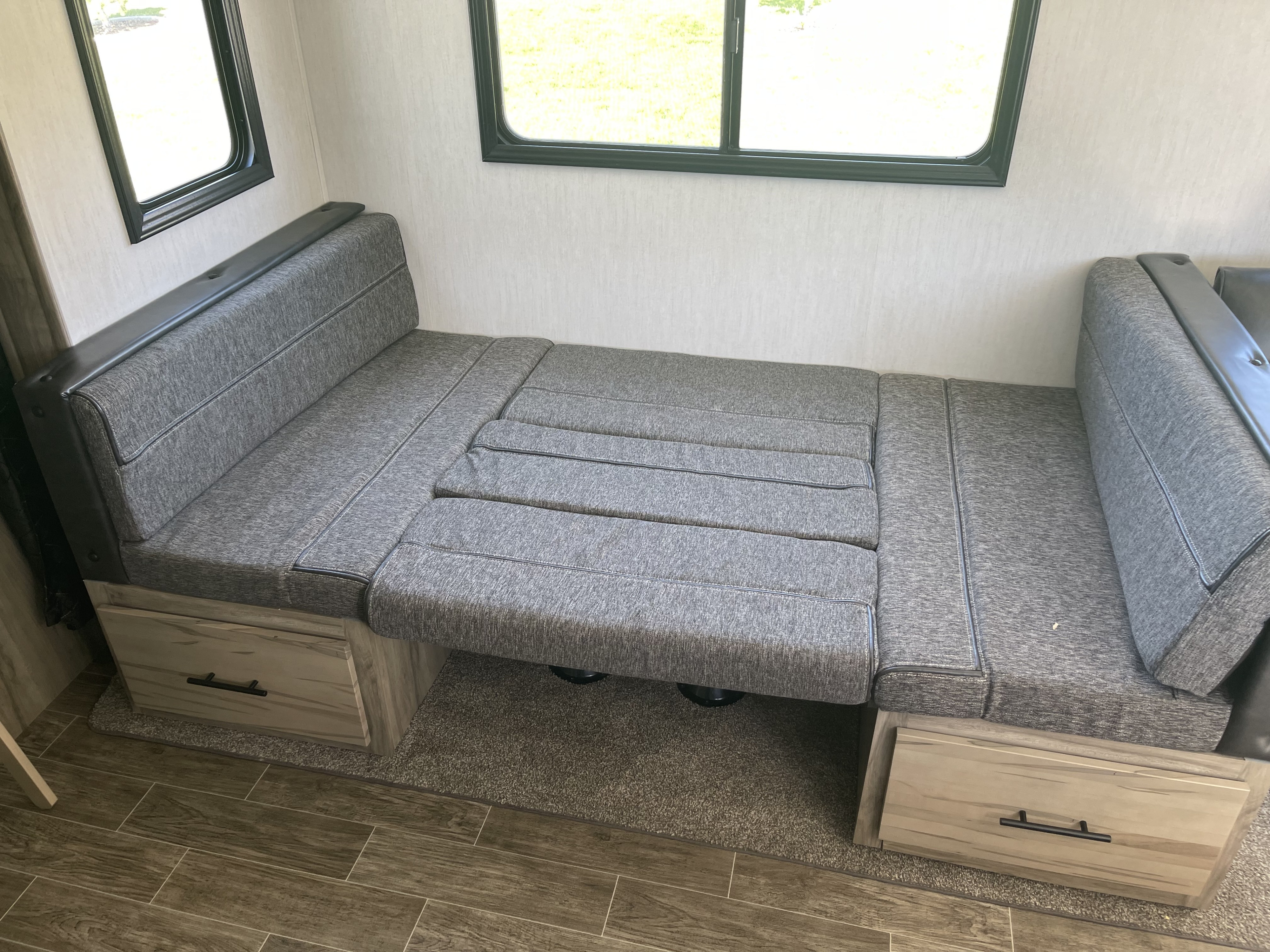 Cozy RV rental interior: grey dinette cushions transform into a bed, with storage drawers and large windows for light.. Forest River Cherokee Alpha Wolf 2021
