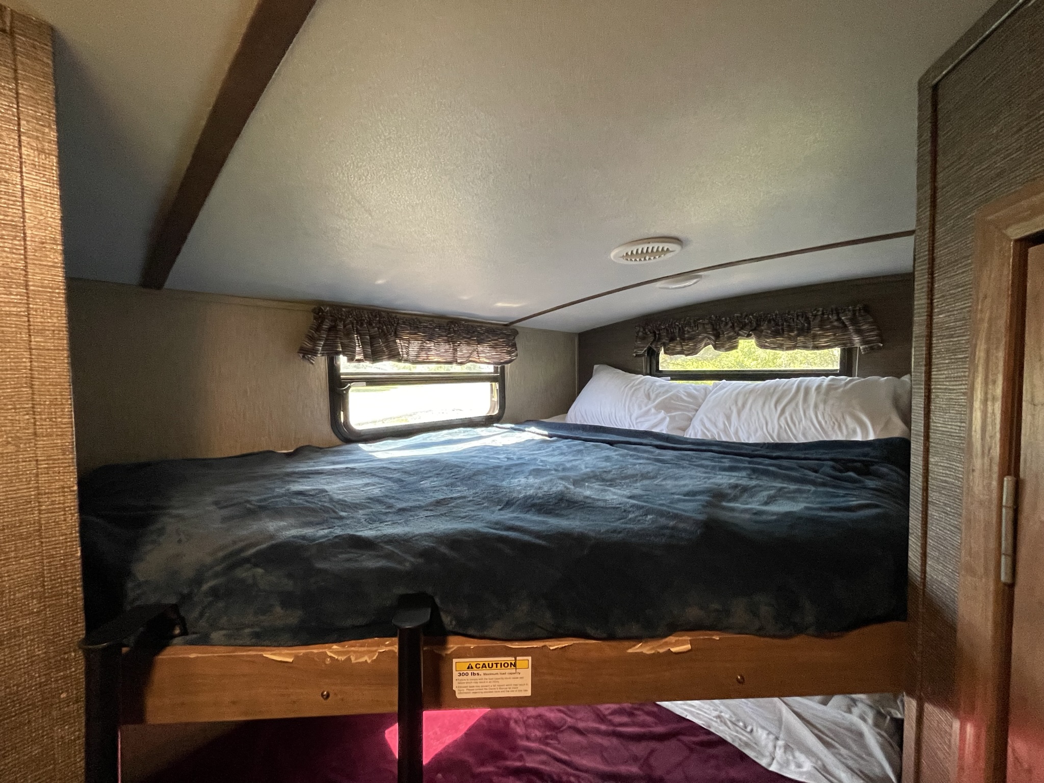 Inside an RV rental: a bunk bed with blue blanket & white pillows, featuring a 300 lb. capacity. Ideal for travel.. Keystone RV Laredo 2016