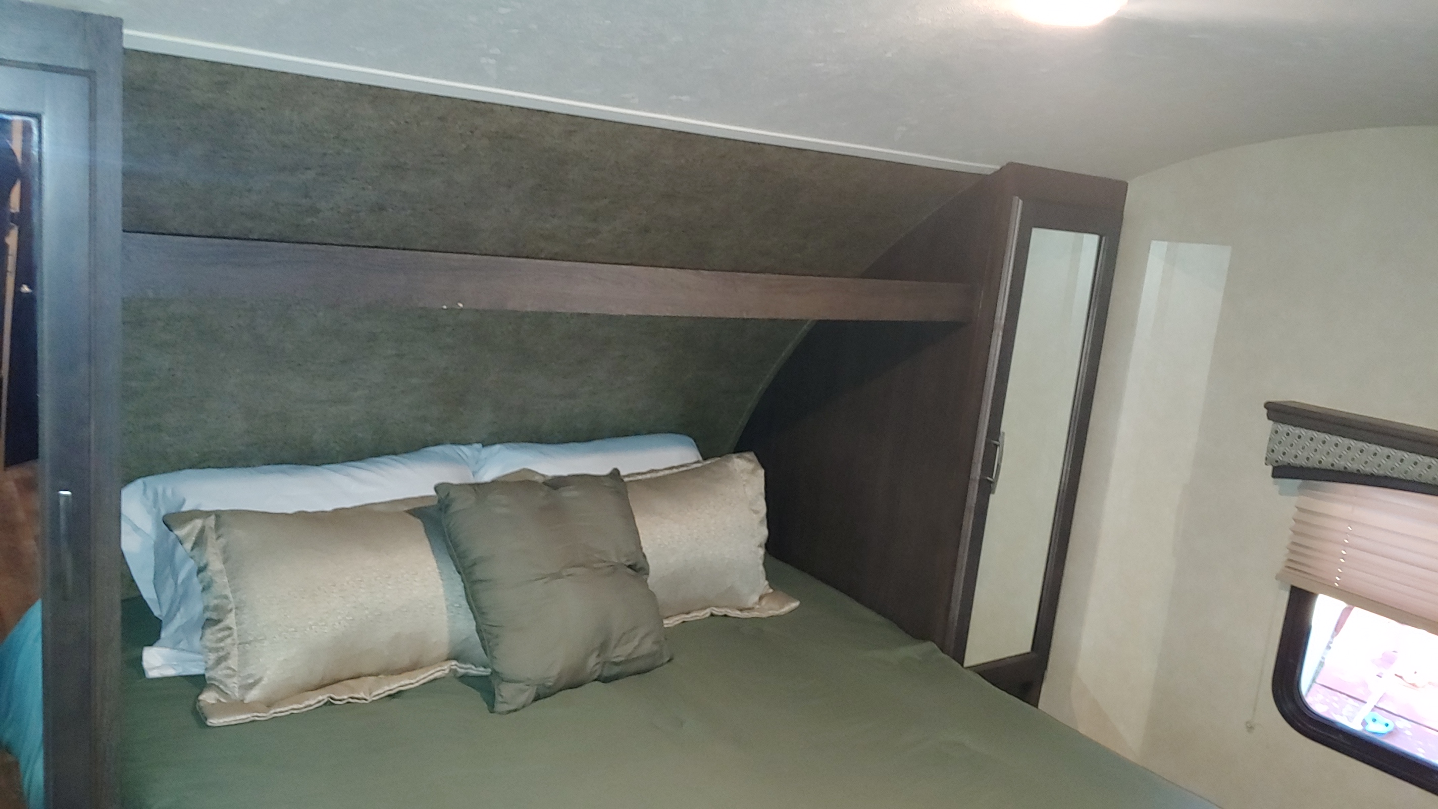 An RV rental bedroom featuring a bed with green linens, pillows, overhead storage, a mirrored cabinet, and a window.. Forest River 2017 sonoma 240bhs 2017