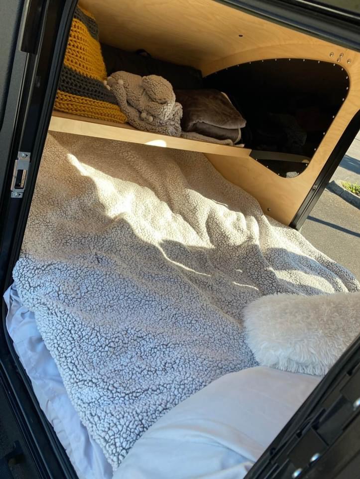 Cozy RV rental interior: bed with sherpa blanket, pillows, and a wooden shelf with storage. Perfect for travel.. Oregon Trail’r DoDrop Alpha 2018