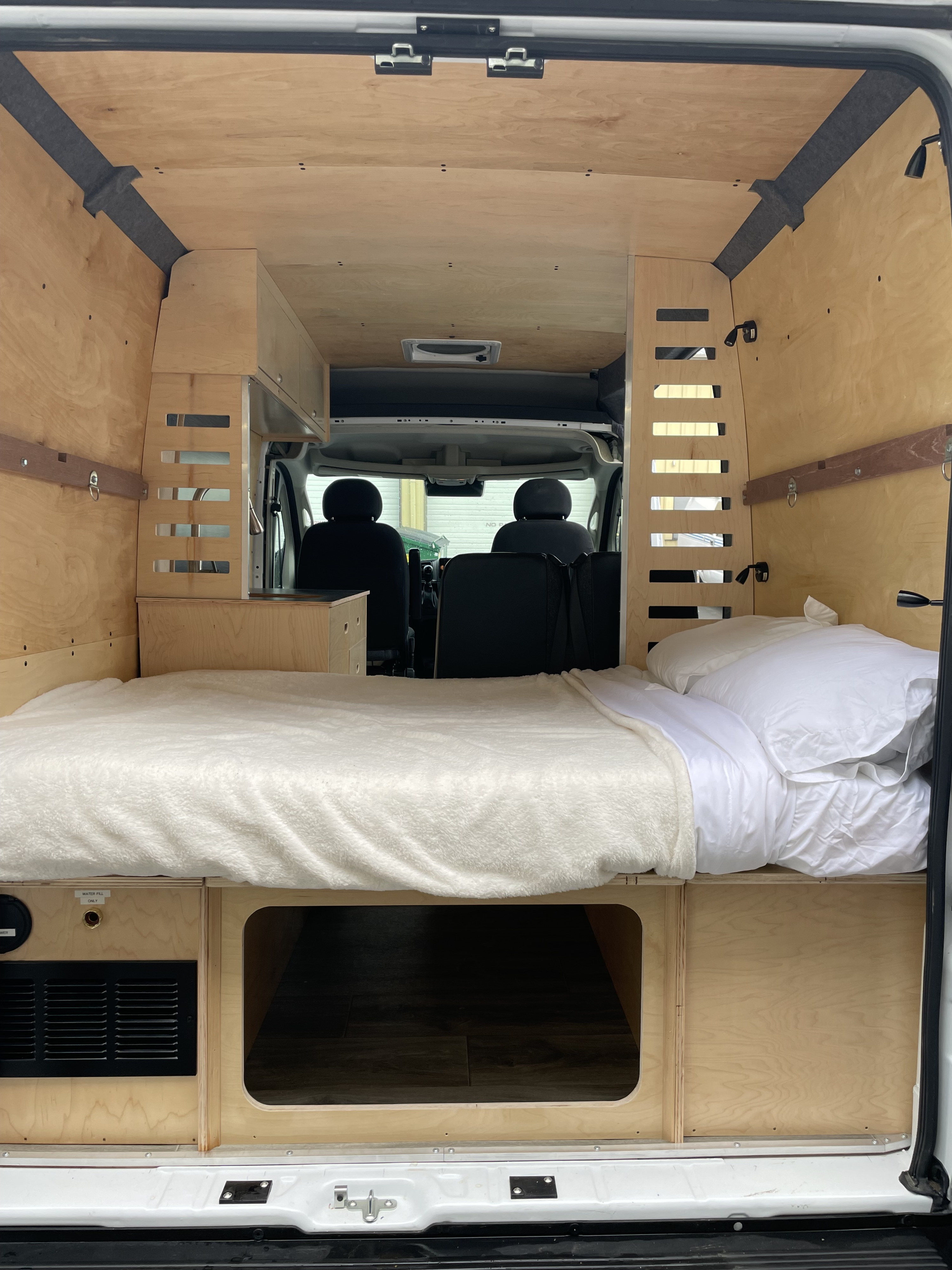 Spacious rv rental interior: custom wood camper van with cozy bed & storage, looking forward to front seats.. RAM ProMaster 2022