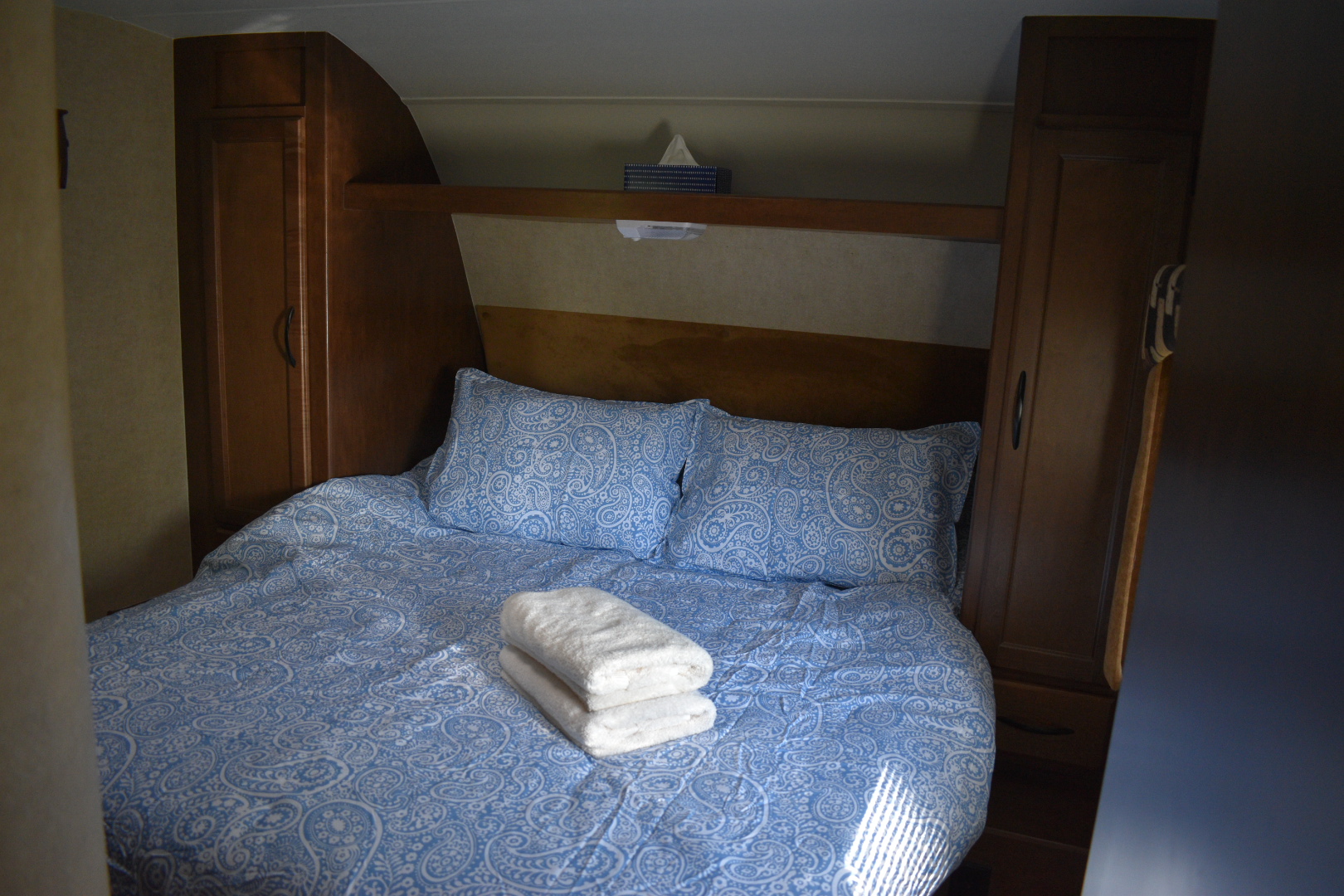 Comfortable rv rental bedroom with blue paisley bedding, fresh white towels, and functional wooden cabinets. Compact and cozy.. Pacific Coachworks Northland 2016