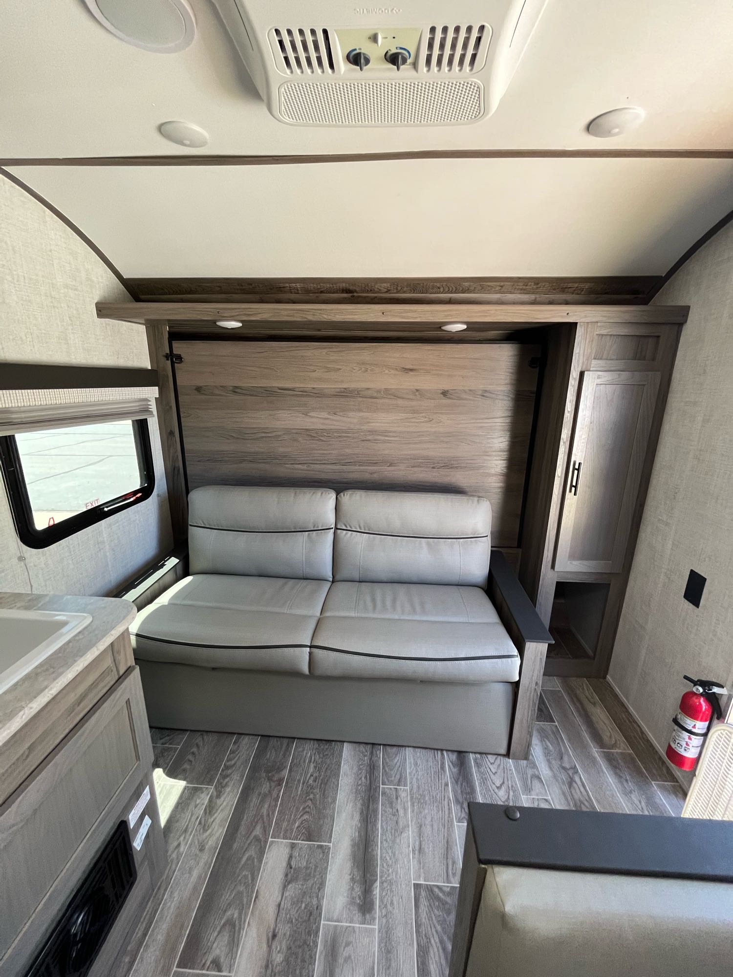 Bright RV rental interior with a gray pull-out sofa bed against wood paneling, compact kitchen, and a fire extinguisher visible.. Gulf Stream Other 2022