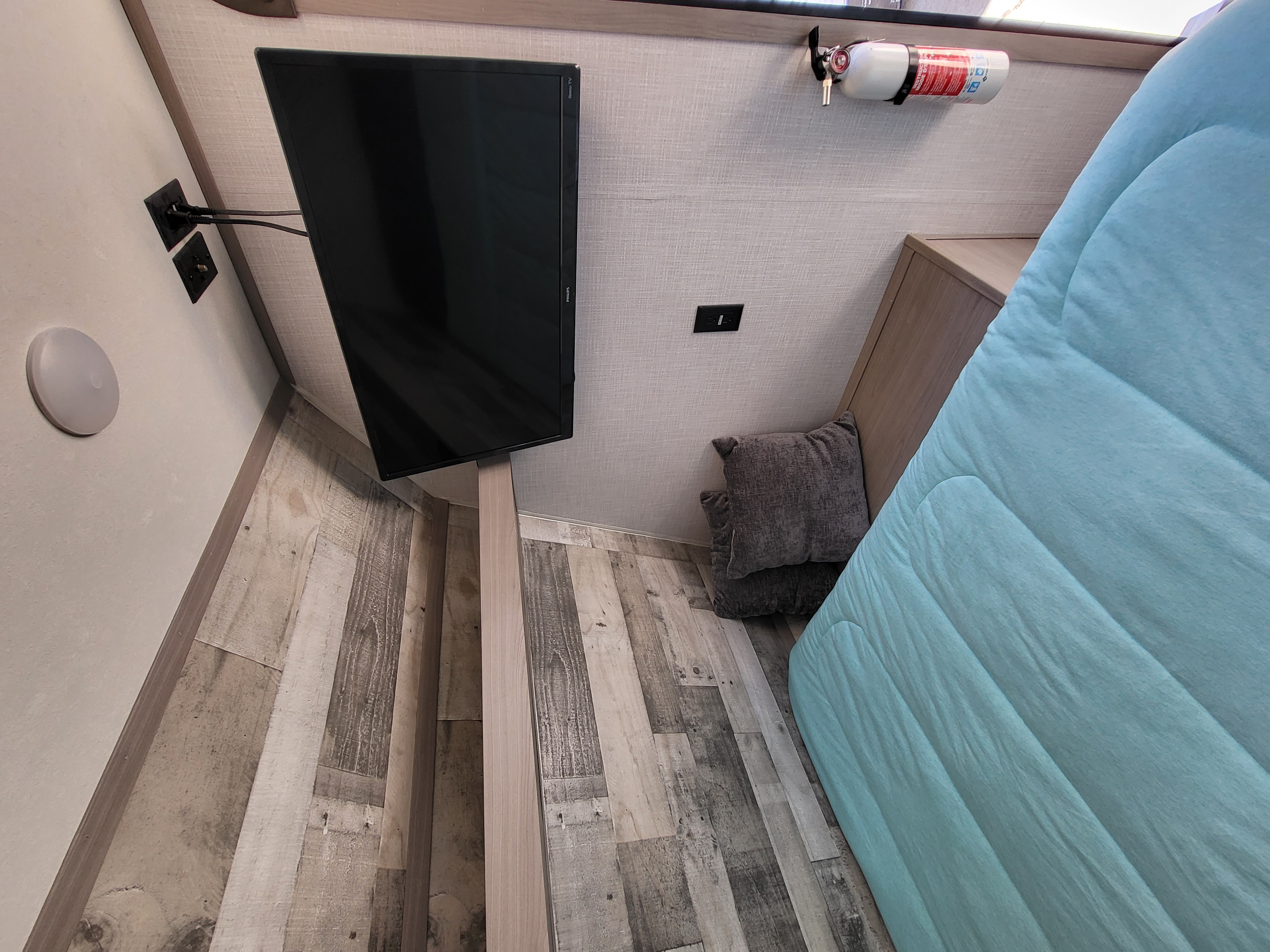 Compact RV rental living space with a wall-mounted TV, blue comforter, and safety-essential fire extinguisher.. Dutchmen Coleman Lantern LT 2022